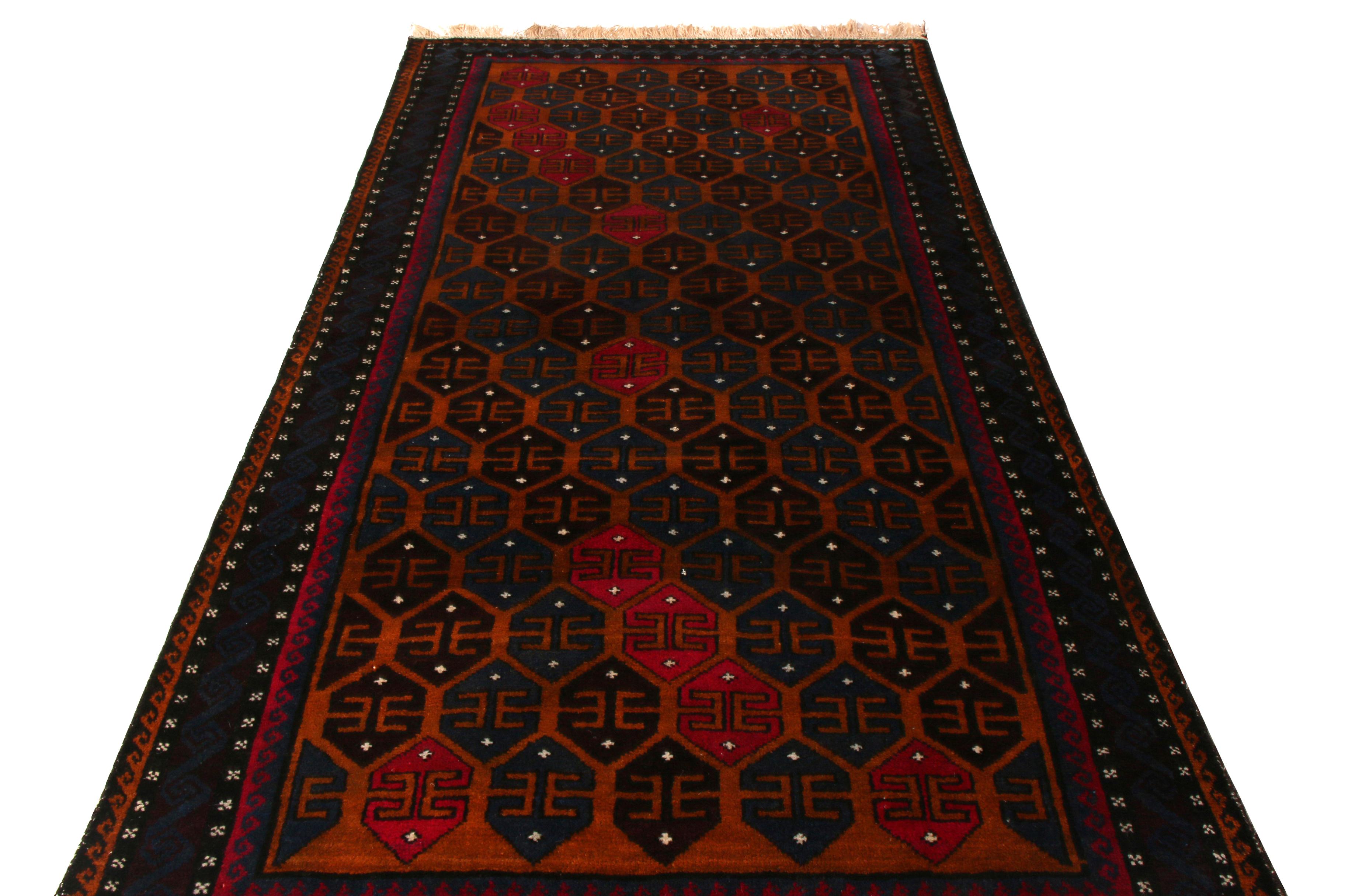 Hand knotted in wool originating circa 1950-1960, this vintage midcentury Persian rug hails from the Baluch tribal weavers of renown, enjoying a play of versatile size and a unique navy blue emphasis in the play of rich brown and red colorway, a