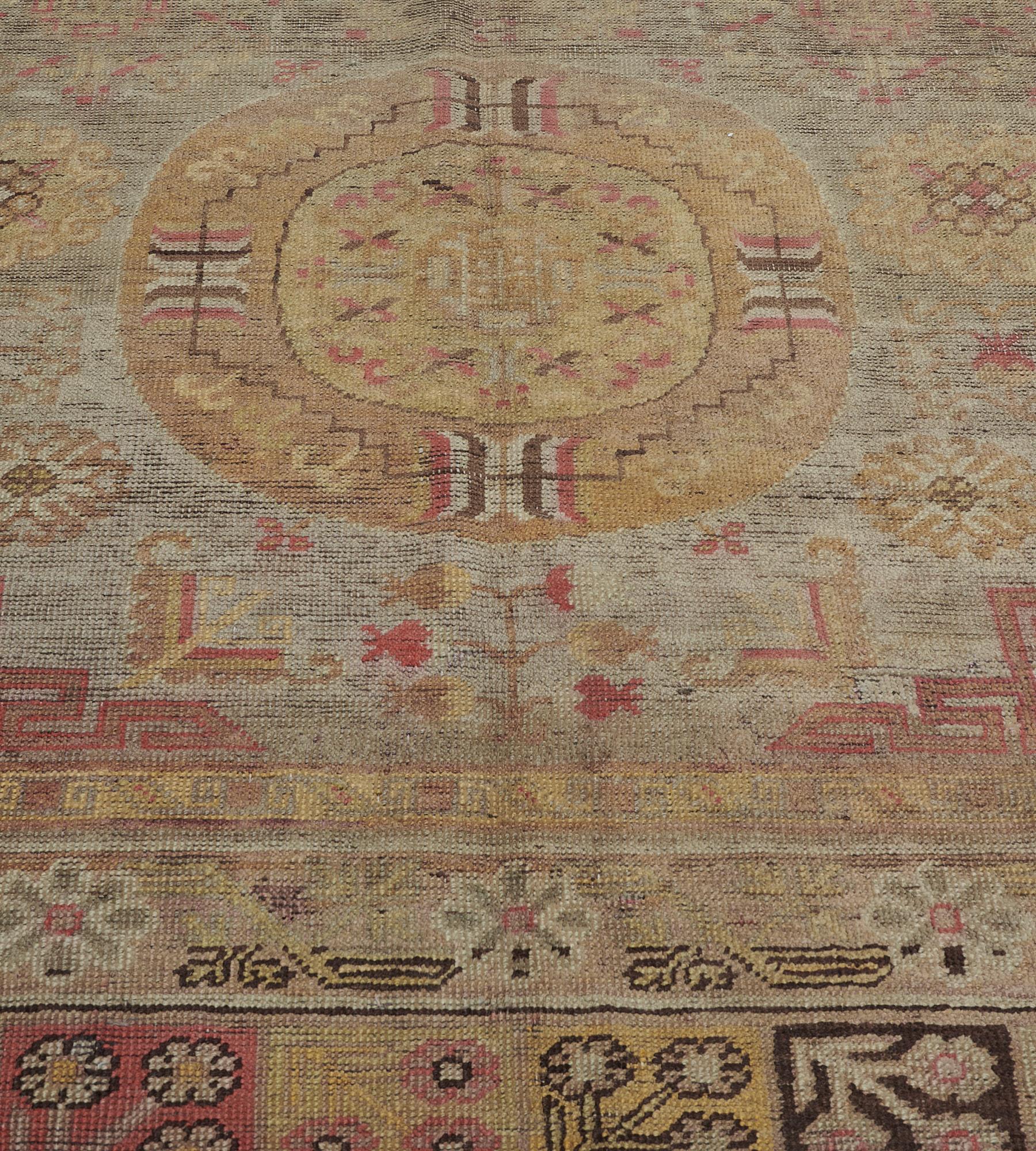 This antique, circa 1870, Khotan rug has a steel-blue field scattered with a variety of flowerheads and further floral motifs around a column of three mustard-yellow and pale brown roundels, the central roundel containing a hooked lozenge with