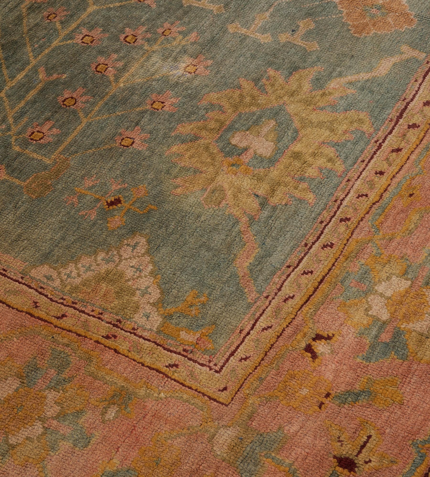 This antique, circa 1880, Oushak rug has a sea-blue field with an overall design of dusty-pink, pistachio-green and aubergine-purple angular palmette and floral vine, in a dusty-pink border of pistachio-yellow and sea-blue palmette and flowerhead