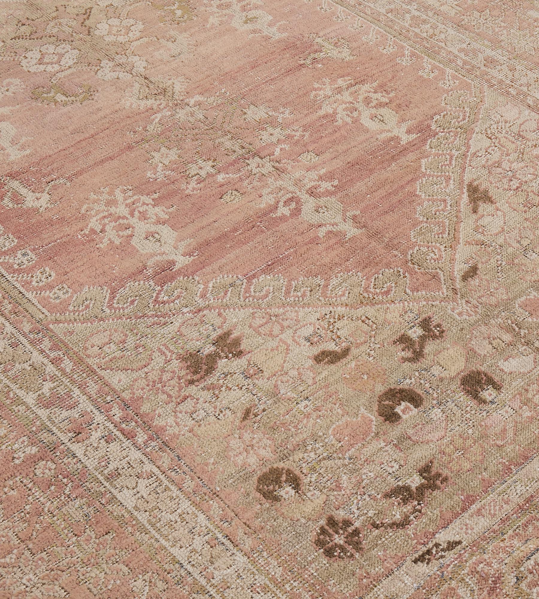 This antique, circa 1880, Ghordes rug has a light salmon-pink field with a central with a central cruciform open lozenge surrounded by a variety of floral motifs and an outer band of ivory rosettes with flowering vases above and below, the light