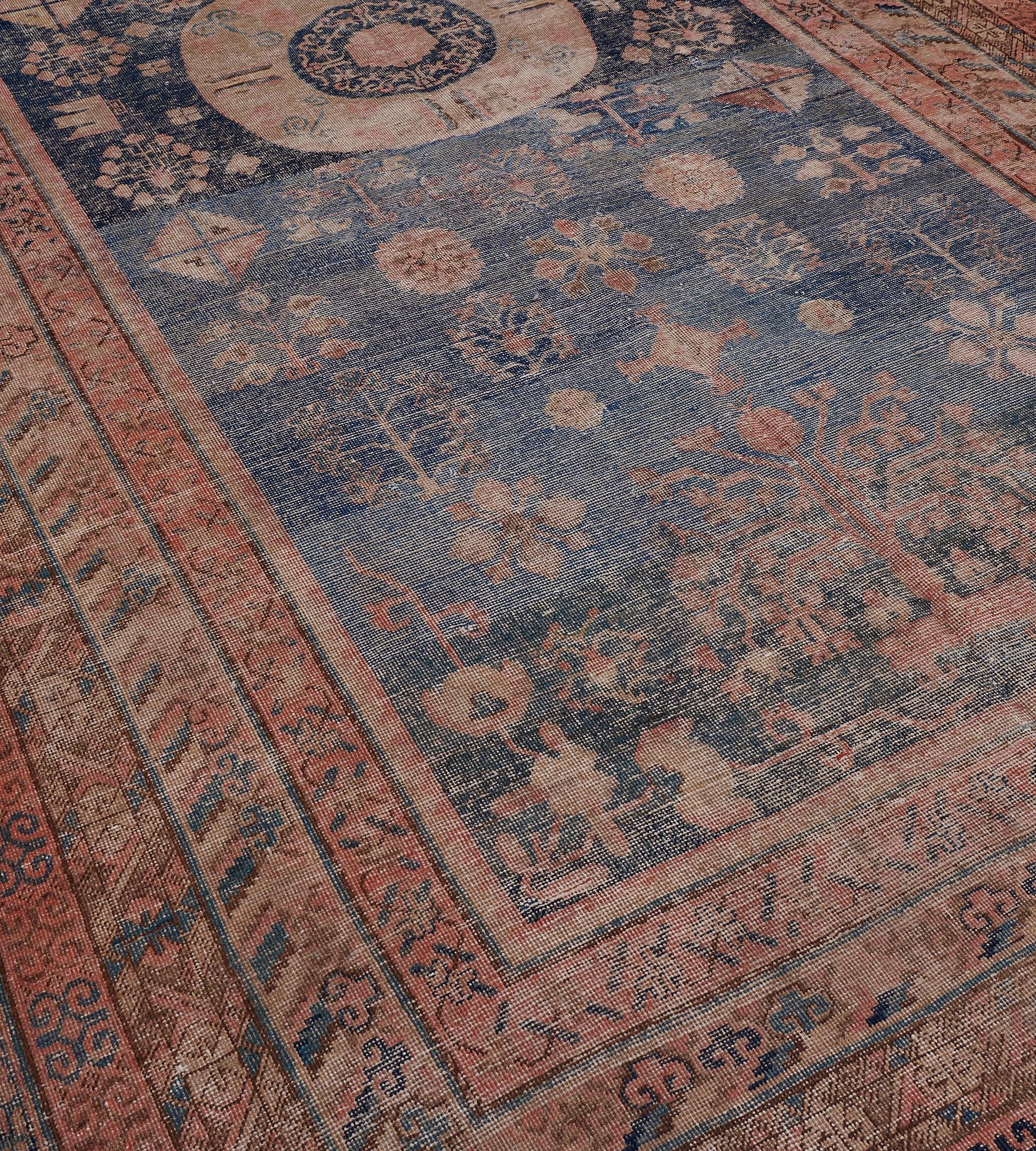 Dieser antike Khotan-Teppich um 1880 hat ein tiefes indigoblaues Feld, das mit einer Vielzahl von Blumenmotiven und blühenden Vasen um ein zentrales Rautenmedaillon mit einer indigoblauen zentralen Rosette verstreut ist, die einen Blumenkopf und ein