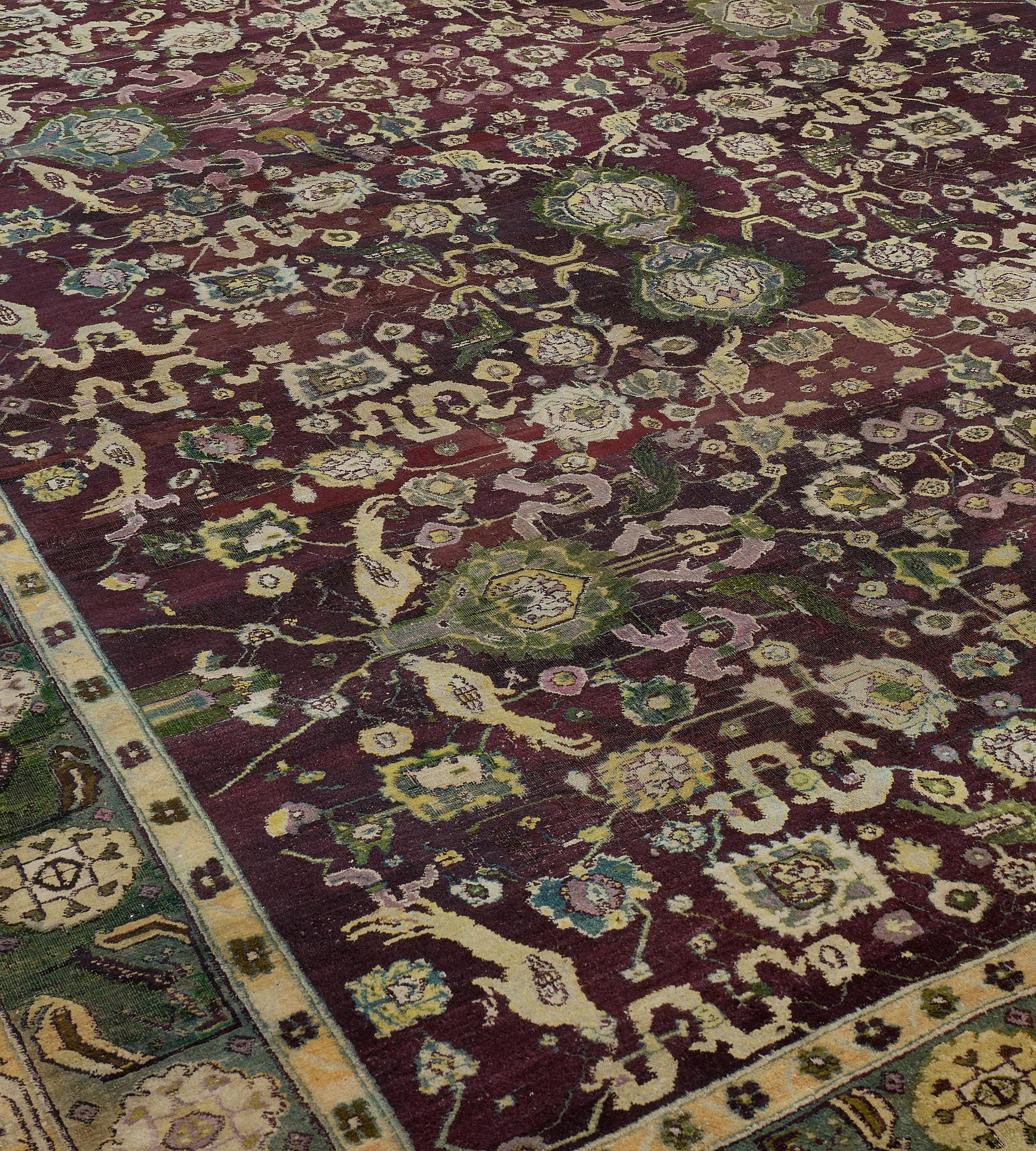 Dieser antike Agra-Teppich aus der Zeit um 1900 hat ein burgunderrotes Feld mit einem Gesamtmuster aus meergrünen, elfenbeinfarbenen und staubrosa Palmetten und Blumenranken mit paarweise hockenden Vögeln in einer meergrünen Bordüre aus