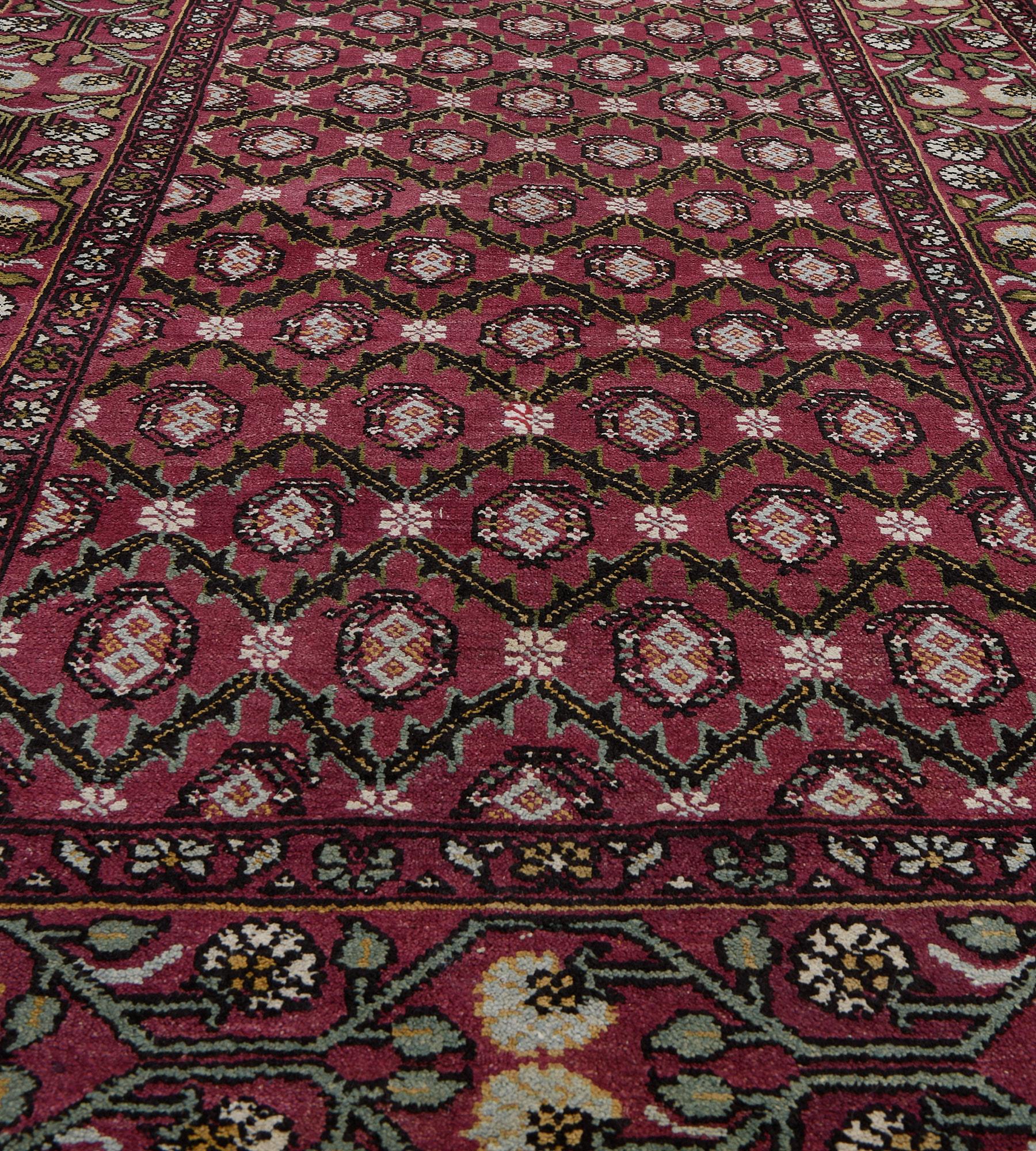 This antique, circa 1900, Agra rug has a burgundy-red field with an overall design of diagonal rows of charcoal-black serrated lozenge vine each lozenge containing a central boteh containing a pair of ice-blue linked lozenges, in a burgundy-red