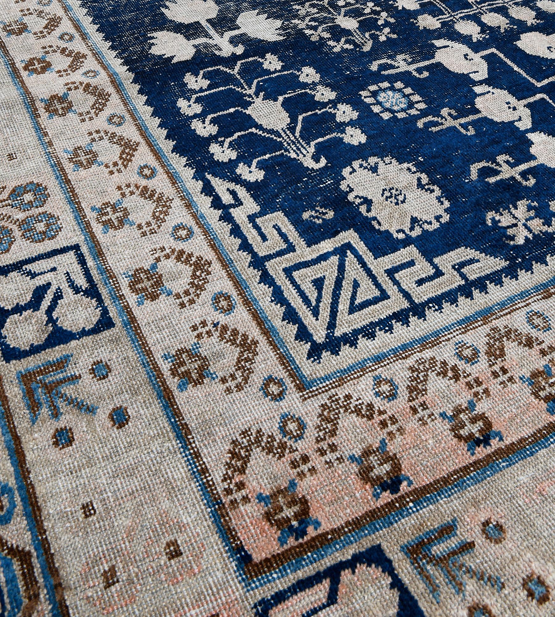 This antique, circa-1900, Khotan rug has a deep indigo-blue field with a central ivory cusped lozenge medallion surrounded by scattered angular floral stems and sprays, the key-pattern spandrels in each corner, in triple striped border the inner