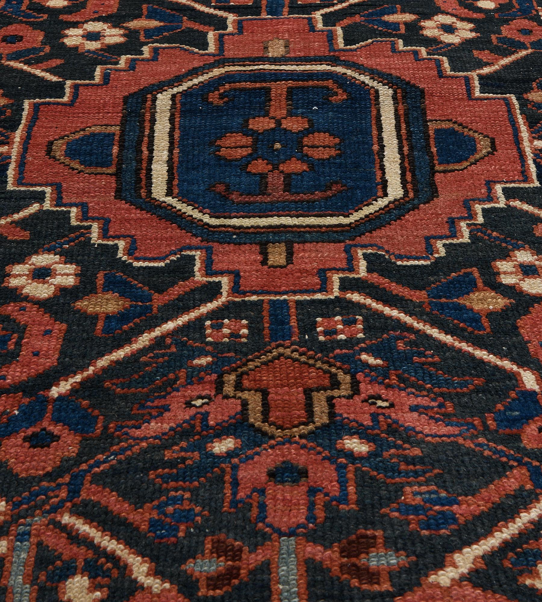 This antique, circa 1900, Heriz rug has a shaded blue field with a central fox-red stepped medallion containing a shaded blue lozenge medallion with an angular hooked floral motif, the medallion issuing a pair of polychrome lozenge palmettes