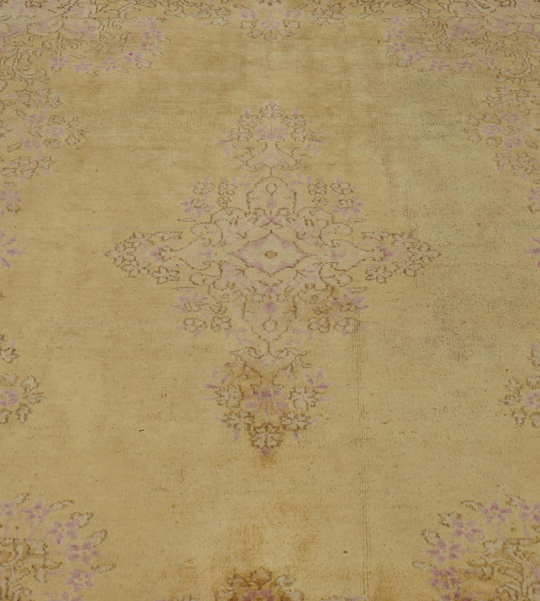 This antique, circa-1920, Kerman rug has a pistachio-yellow field with a central delicate floral lozenge with floral pendants, scrolling shaded pink and olive-green spandrels in each corner, in a broad similar scrolling floral border within a