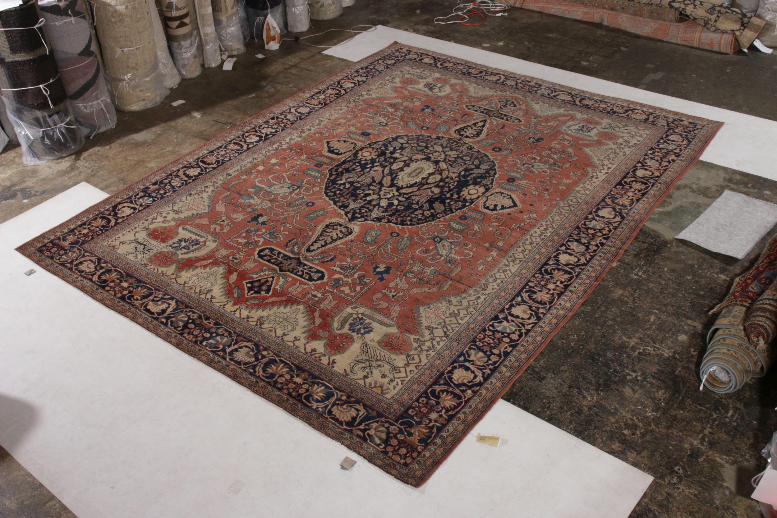 Noué à la main en laine et datant d'environ 1900-1910, ce tapis ancien de 10 x 12 évoque un tapis de Farahan d'une grandeur particulière. Il représente un motif de médaillon royal dans un fond de couleur bleu profond qui accentue le jeu dominant,