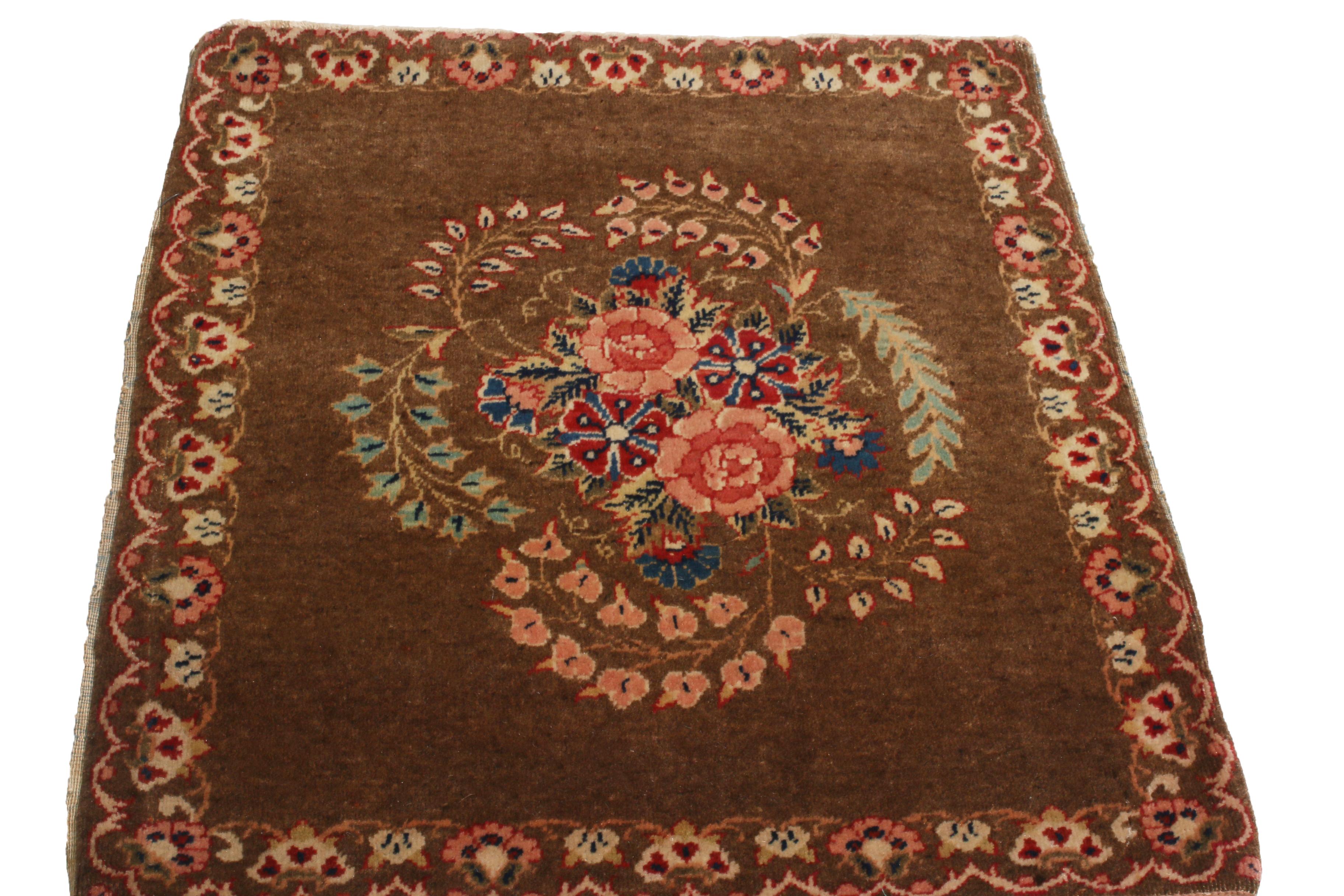 Originating from Persia in 1900, this hand-knotted wool antique Persian rug enjoys a distinguished classical combination of rich brown, vivid pink, and bright green colorways throughout an abrash field, complemented by highly stylized carnation