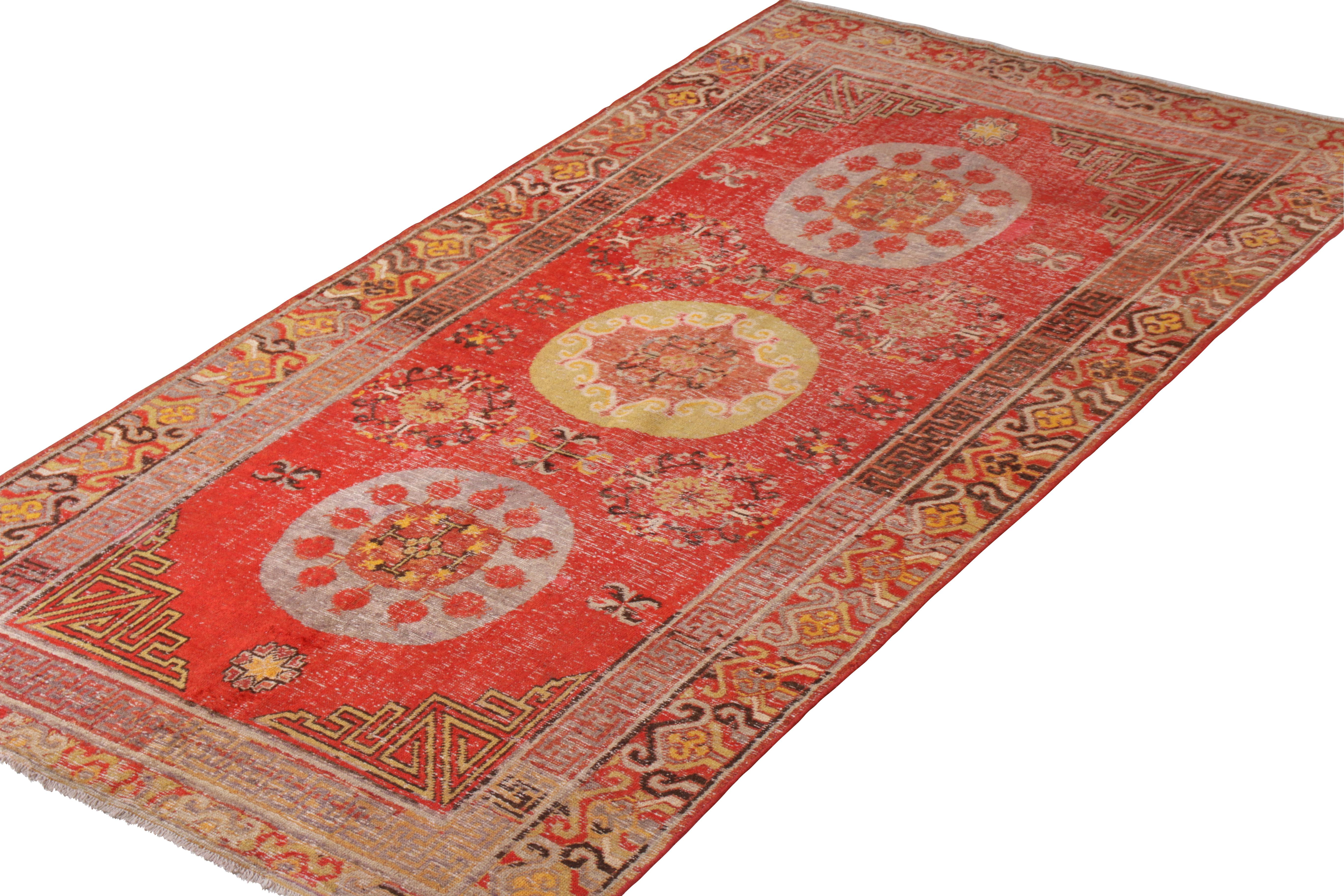 An antique 6 x 11 Khotan rug in red and gold, enjoying rosette medallion patterns celebrated in this renowned oriental style. Hand knotted in wool, aged into a handsome distressed aesthetic complementing the traditional style in this classic piece.