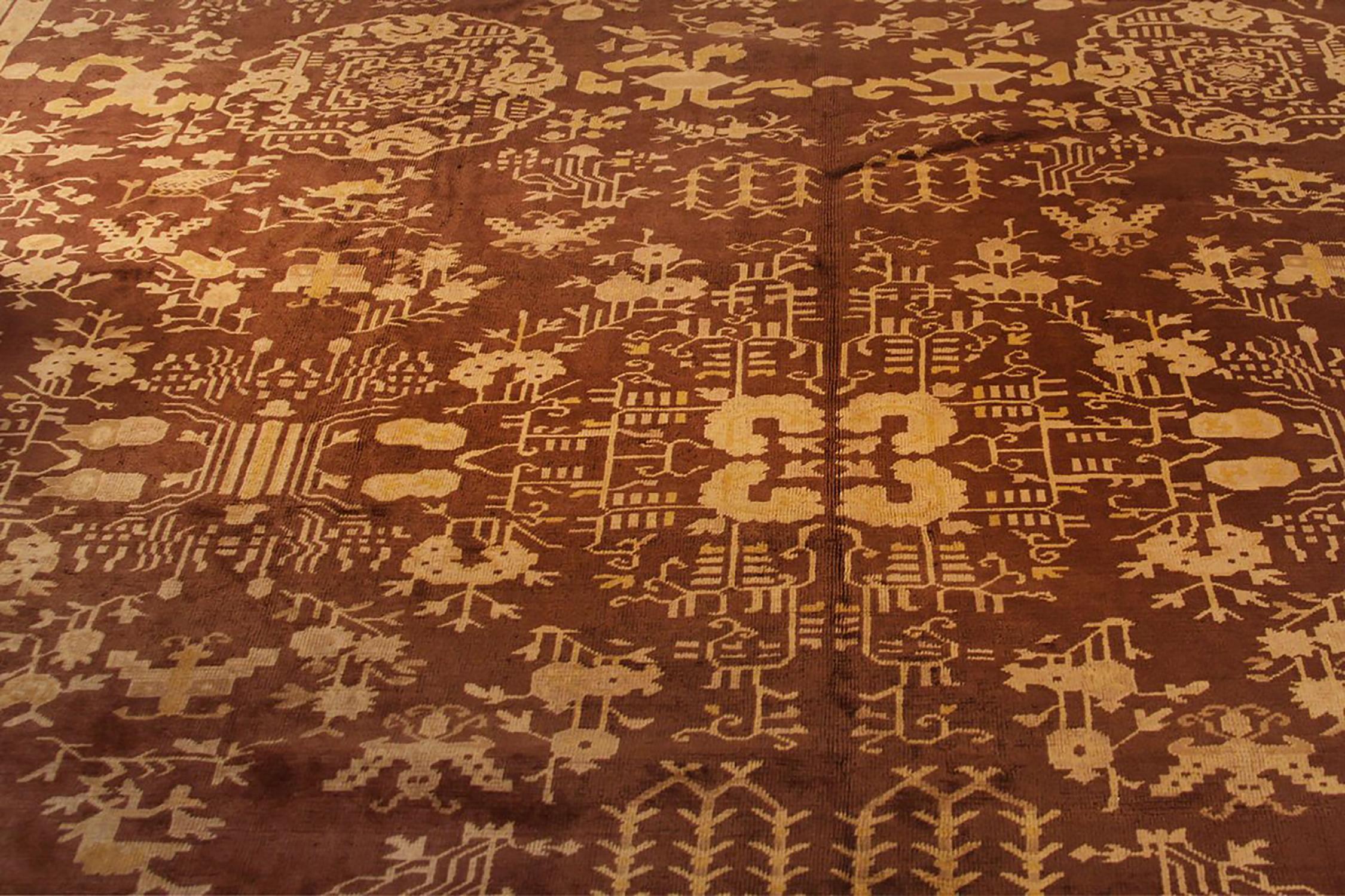Hand knotted in wool originating from East Turkestan circa 1910-1920, this antique rug is a rare 12 x 16 Khotan rug seldom seen in both this magnificent scale and rich beige brown colorway hues. 

On the design: The atypical approach to scale