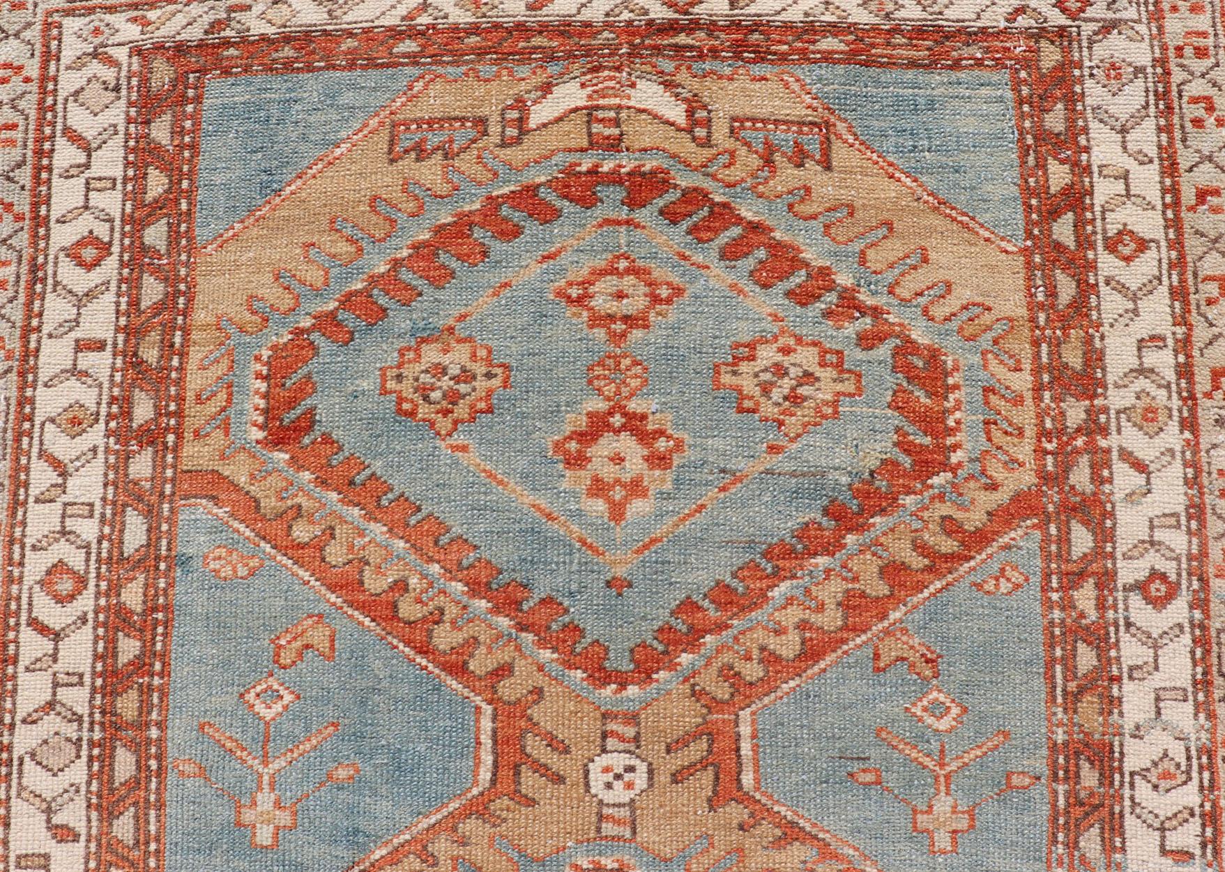 This antique Persian Karajeh runner features a tribal sub-geometric triple medallion design rendered in multicolor, set upon a blue background. A complementary, multi-tiered border encompasses the entirety of the piece; making it a marvelous fit for