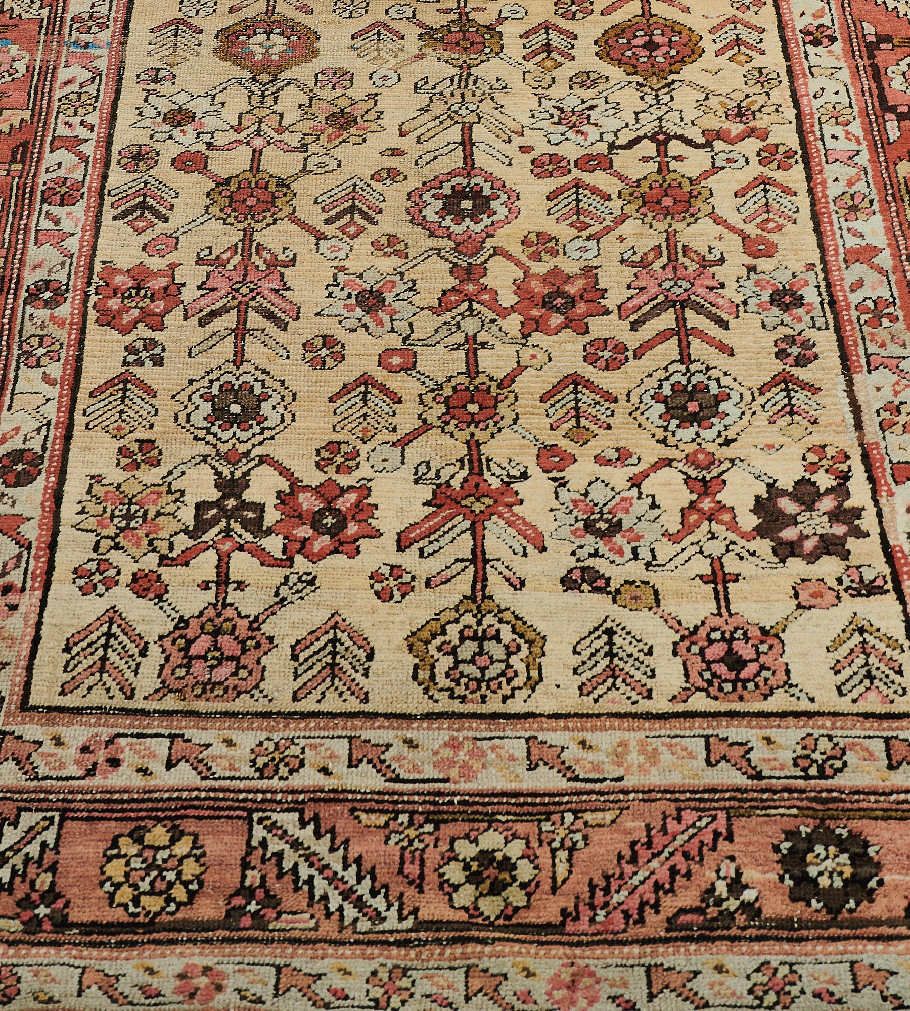 This antique Heriz runner has a sandy-yellow field with an overall design of polychrome columns of angular palmette and floral vine scattered with serrated leaf and floral stems, in shaded terracotta-red serrated leaf and palmette vine border