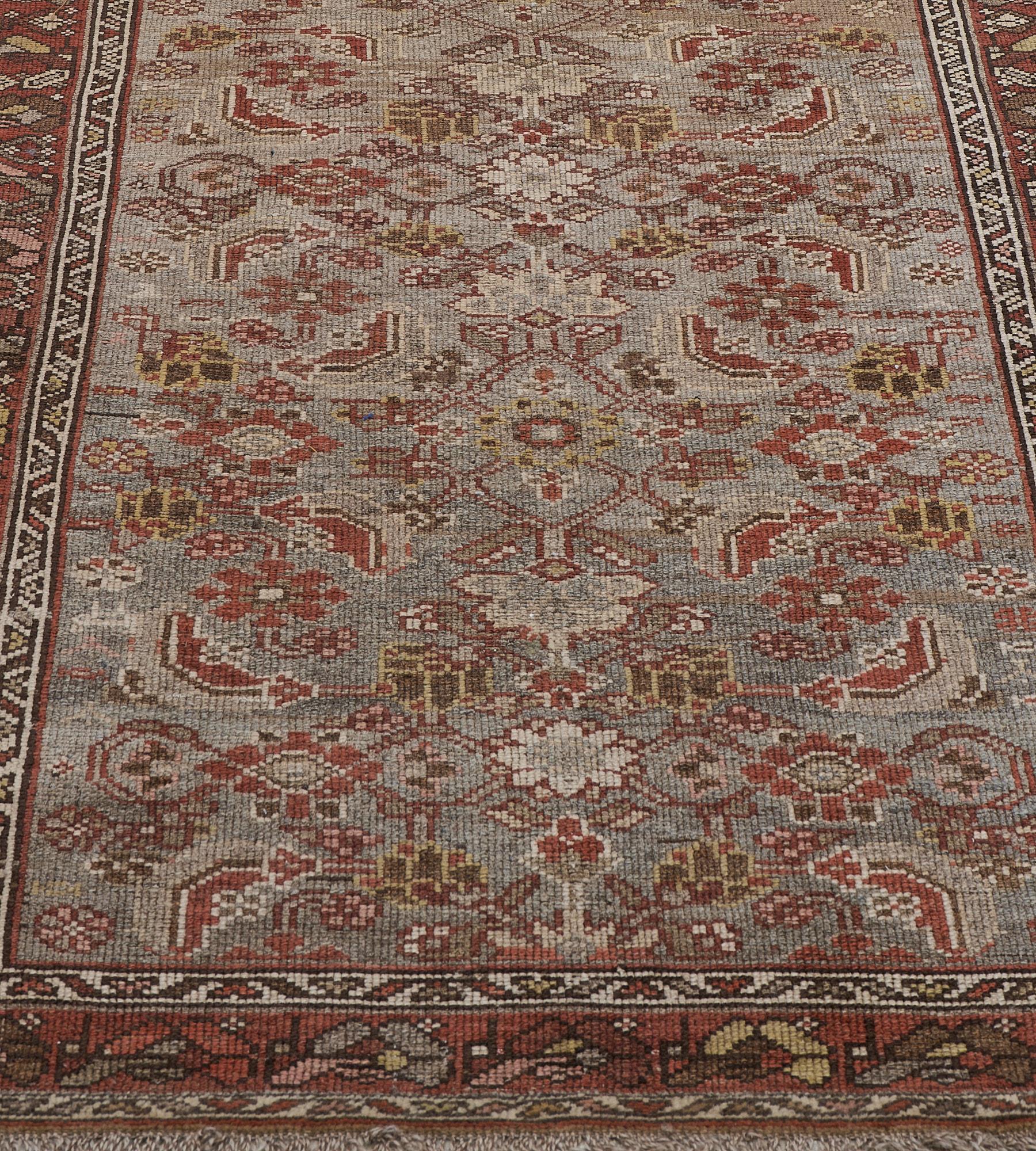 This antique Persian Malayer rug has a shaded steel-blue field with an overall fox-red, sandy-yellow, ivory and shaded pink herati-pattern, in a fox-red border of polychrome linked floral motifs between ivory ribbon floral vine stripes.