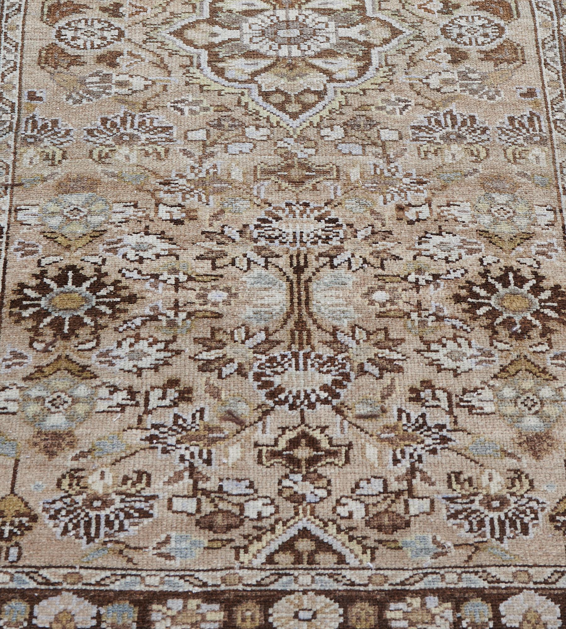 This antique Malayer runner has a buff-brown field with a column of mole-brown cusped medallions each containing a central rosette and floral sprays, surrounded by a dense mole-brown, fox-brown, pistachio-green and ivory floral vine, in a mole-brown