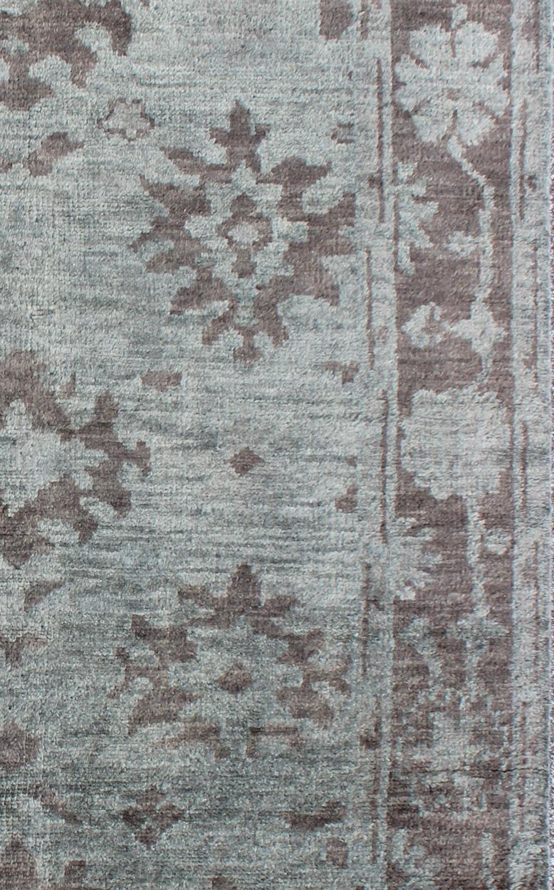Mesures 5'6 x 8'6 

Ce tapis Oushak floral a été noué à la main avec de la laine indienne dans les années 2010. Le fond du champ central est rendu dans un beau bleu sourd, avec des crêtes florales dans un brun cacao. La bordure inverse les