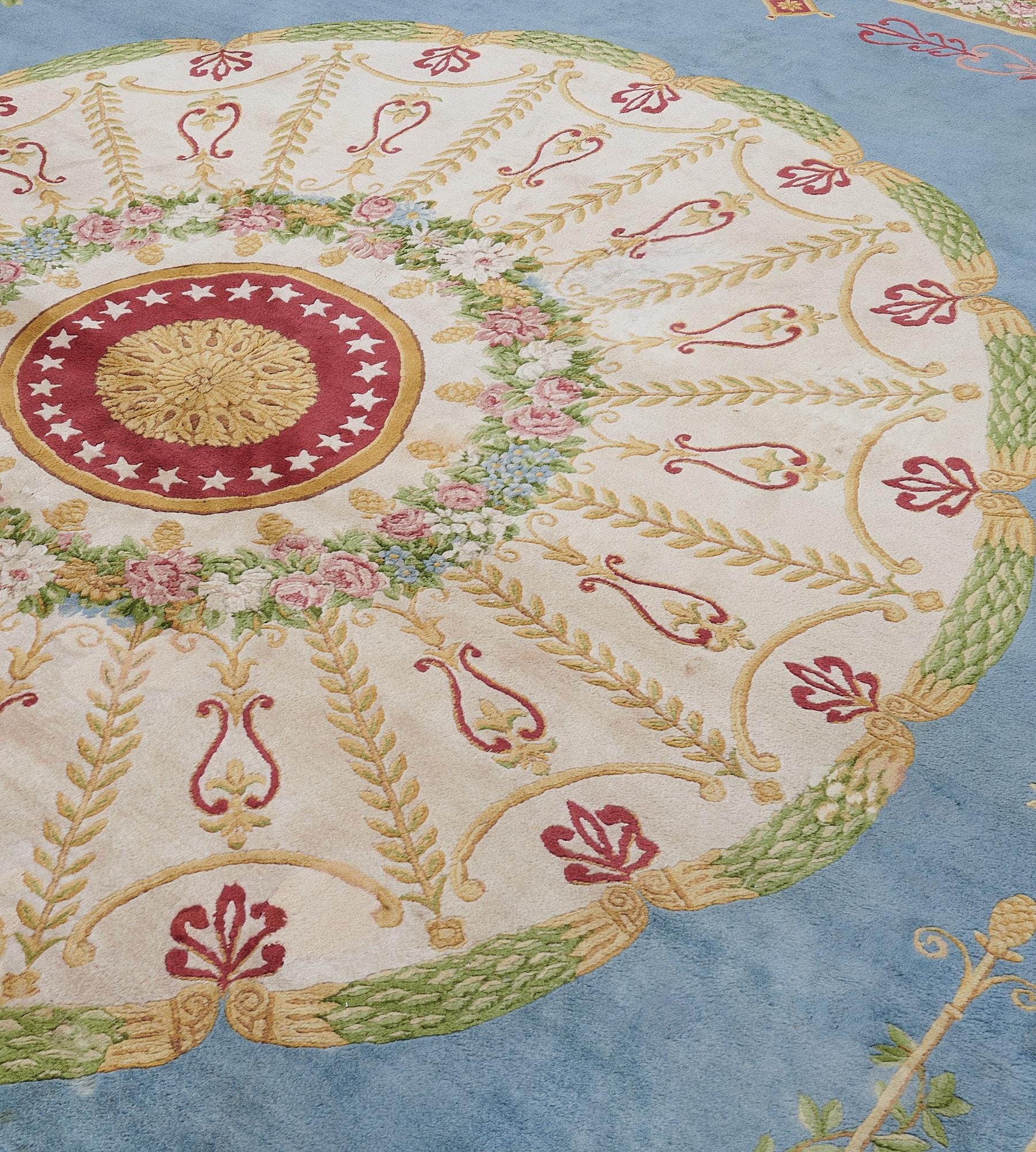 Ce tapis de la Savonnerie a un champ bleu ciel avec un grand rondeau circulaire ivoire et un rondeau central rouge bourgogne avec une feuille d'acanthe dorée au centre, entouré d'une bande d'étoiles ivoire et d'une bande extérieure dorée, entourée