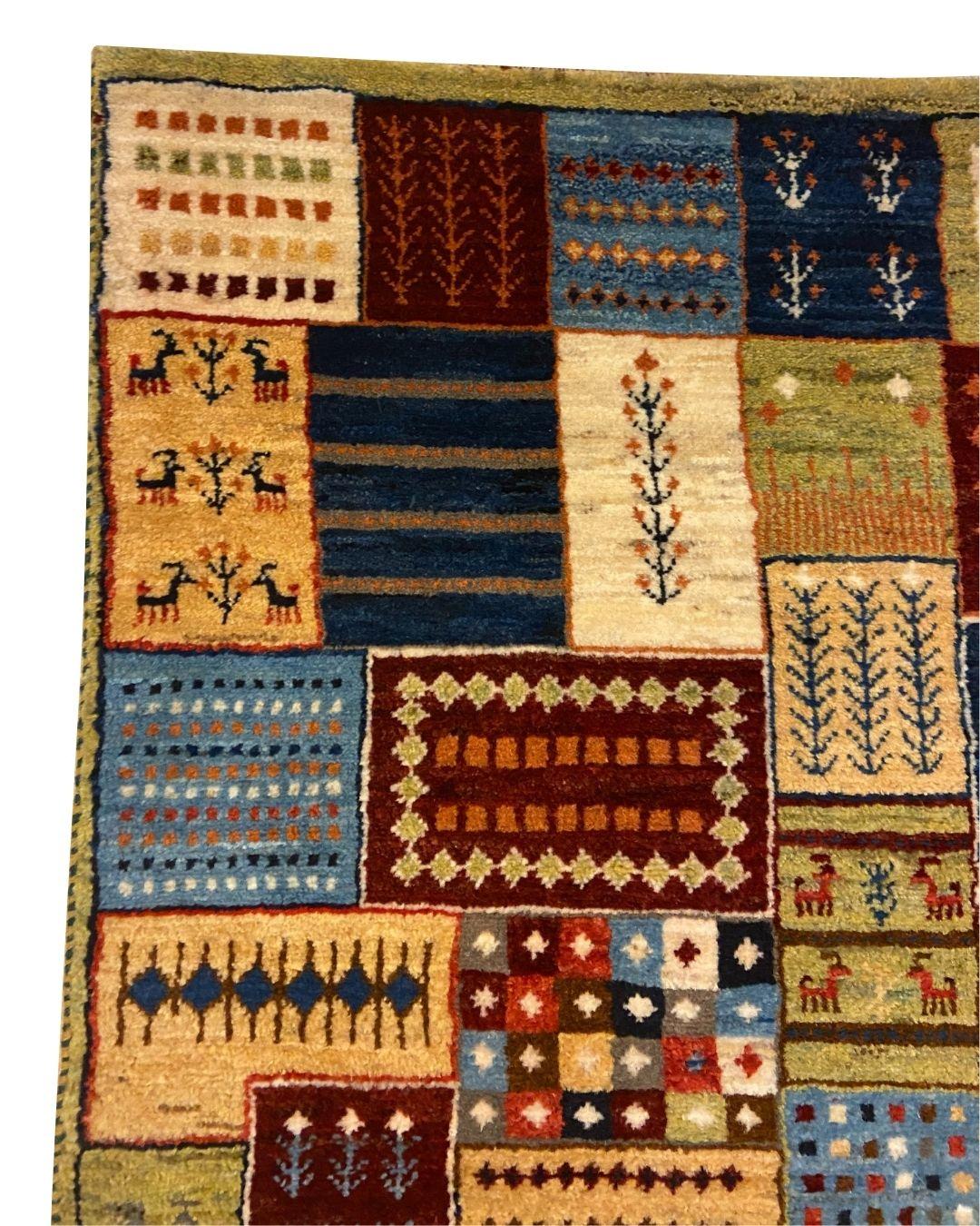 Questo tappeto Gabbeh in lana annodato a mano, che misura 2′8″ × 4′3″, è una celebrazione della tradizione, dell'artigianato e della bellezza dell'imperfezione. Composto da piccoli pannelli con animali stilizzati, alberi e motivi astratti, il design