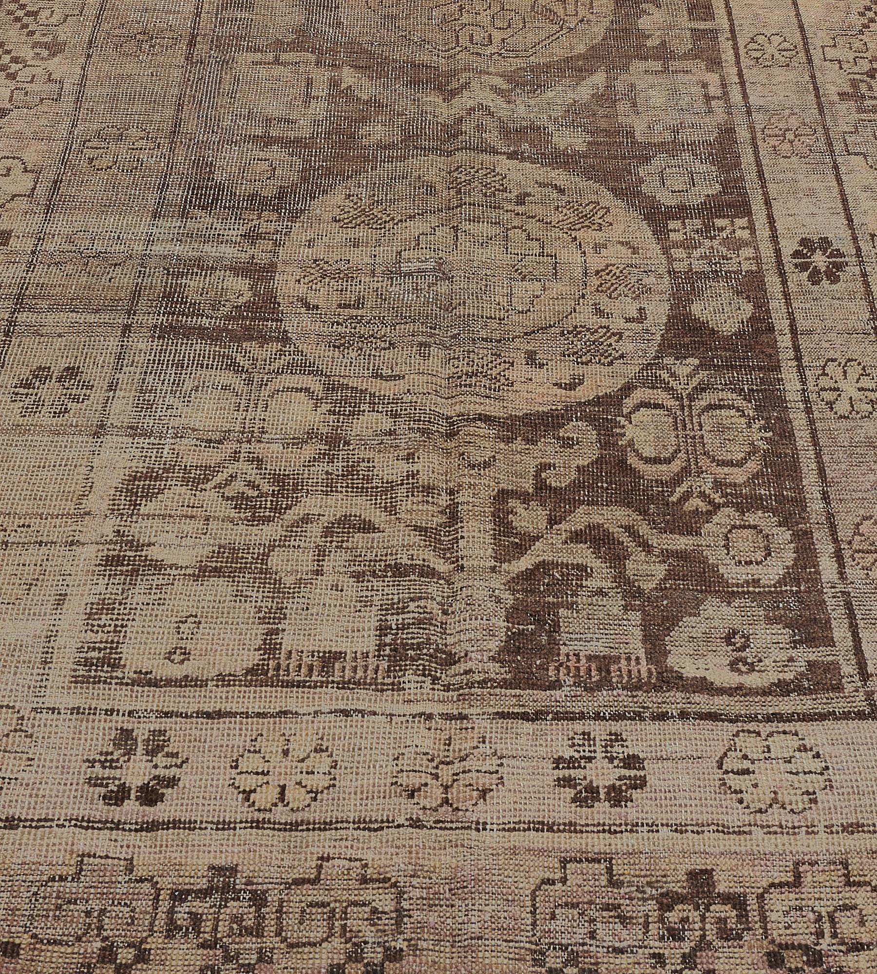 This antique, circa 1880, Khotan rug has a chocolate-brown field with a column of three sandy-yellow roundels containing a central lozenge surrounded by a band of floral motifs and an angular palmette vine in the central lozenge, surrounded by
