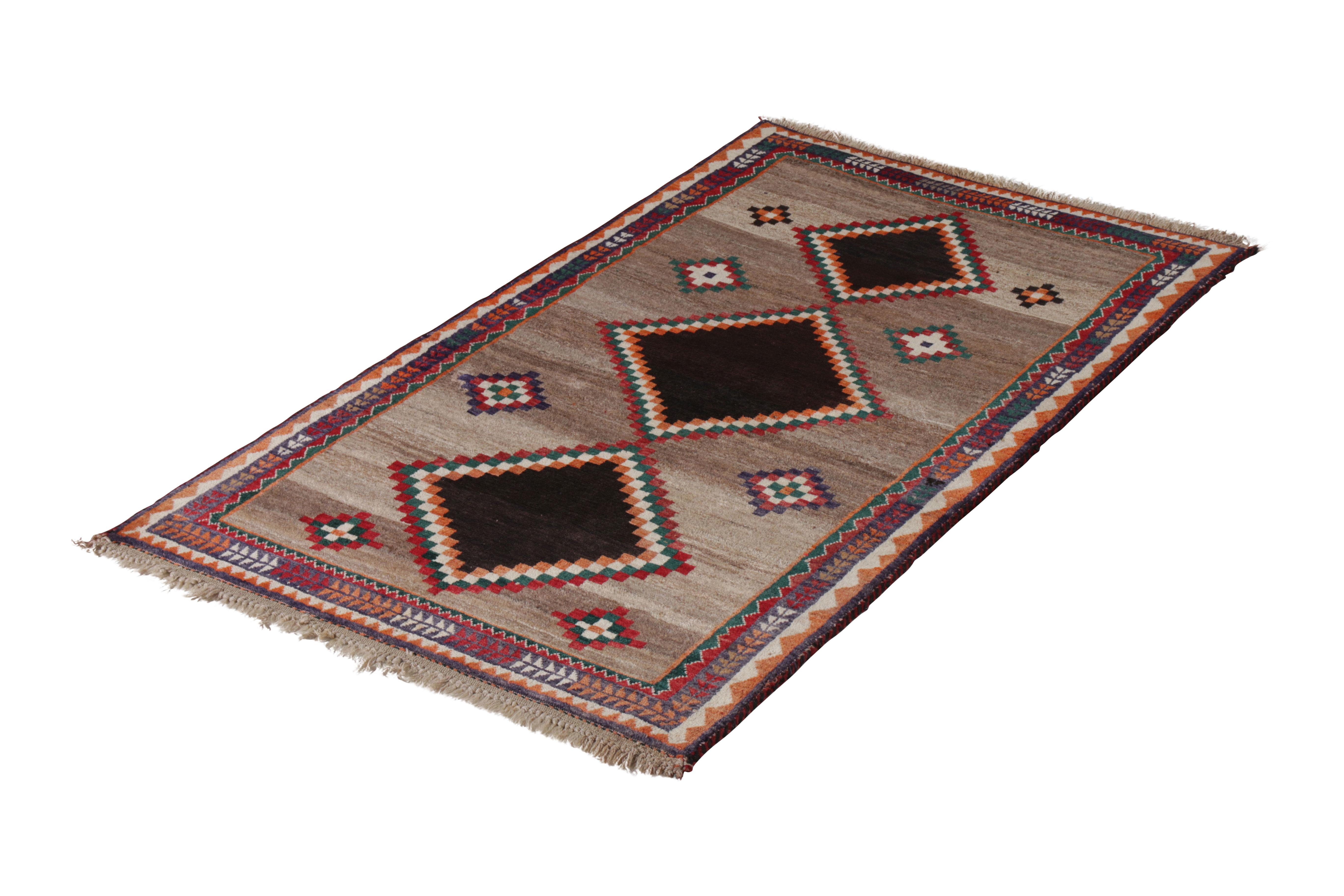 Hand knotted in wool originating circa 1920-1930, this antique Persian rug connotes a tribal Gabbeh rug design marrying a comfortable beige-brown medallion pattern with accenting tribal colorways. The natural dimensionality of the varied earth tones