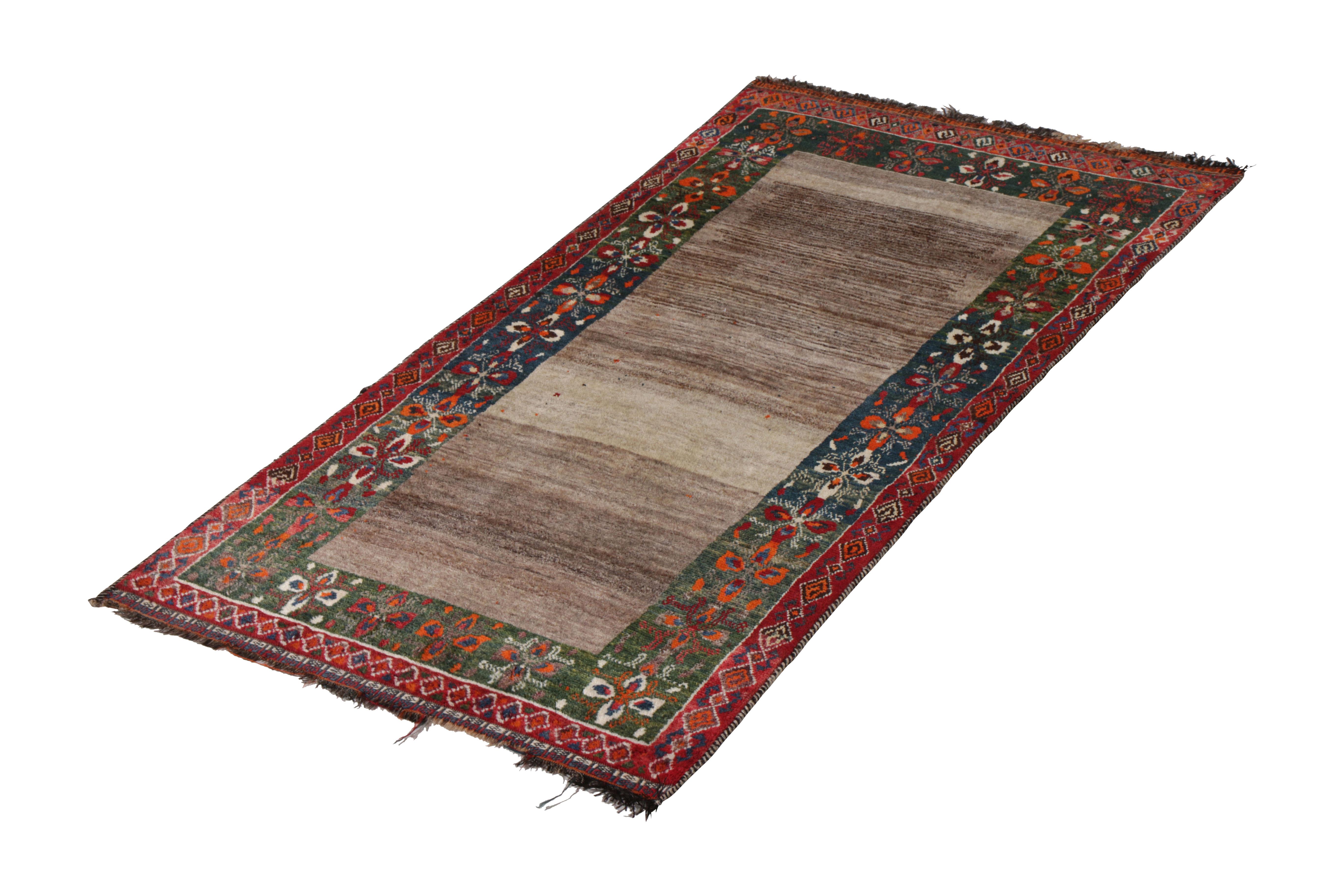 Hand knotted in wool pile originating circa 1950-1960, this vintage Persian rug connotes a midcentury Gabbeh tribal rug design, further remarking a rare play of gray, red, and green colorways with an equally uncommon dual border around the abrashed
