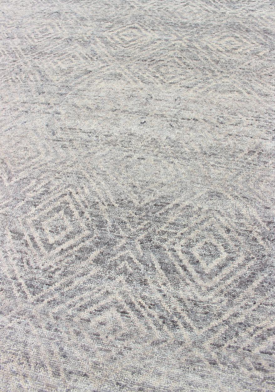 This large Keivan Woven Arts area rug was hand-knotted in India during the 2020s. Common with modern rugs, this Keivan woven arts modern rug displays no borders or flashy colors. The field is rendered in a light smoky gray, with geometric repeating