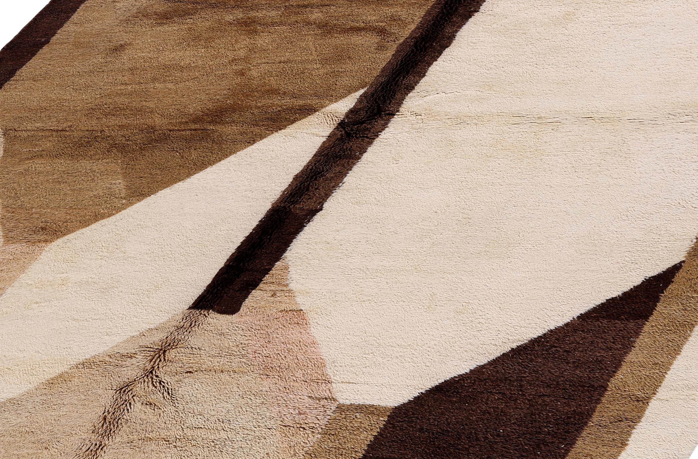 Esta alfombra marroquí anudada a mano es una sorprendente interpretación moderna de la artesanía bereber tradicional, en una cálida paleta terrosa de marrones naturales, marfil y tonos arena. Tejida en lana 100% natural, la alfombra muestra un