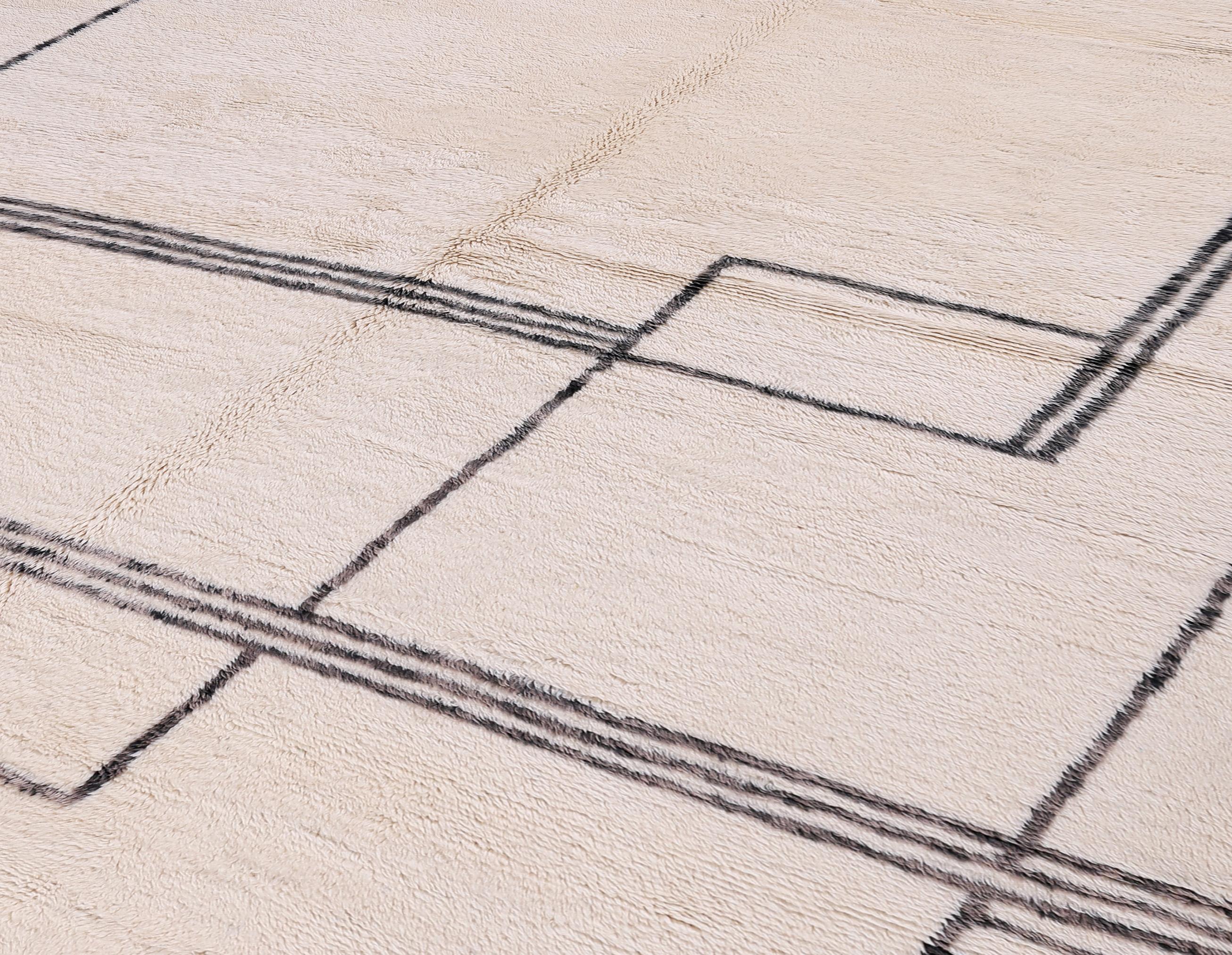 Questo lussuoso tappeto marocchino presenta un'estetica moderna e minimalista, definita da una sorprendente composizione lineare in nero su uno sfondo di lana avorio naturale. Annodato a mano da artigiani berberi con lana pregiata e non tinta,