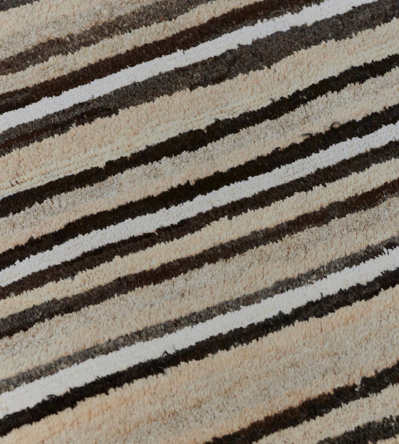 Esta alfombra turca Deco de pelo profundo, tejida a mano, tiene rayas de anchura variable de color beige, marfil, carbón y negro.