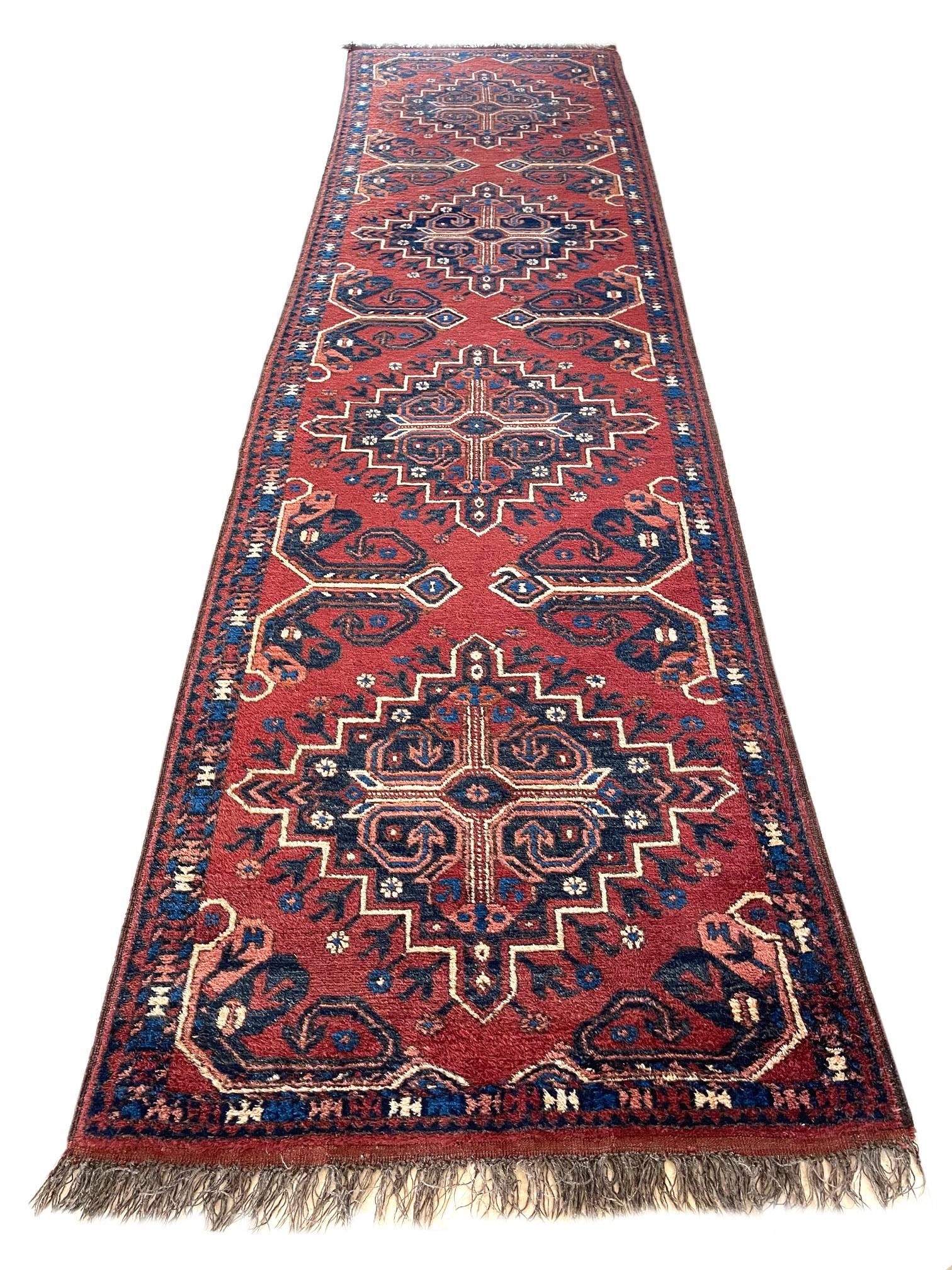 This runner is an Afghan rug which is a workshop carpet woven by a weaving house in Afghanistan. Afghanistan has a rich history in the craft of rug-making. The design in this piece is tribal with repeated medallion. Rich rust color with cream and