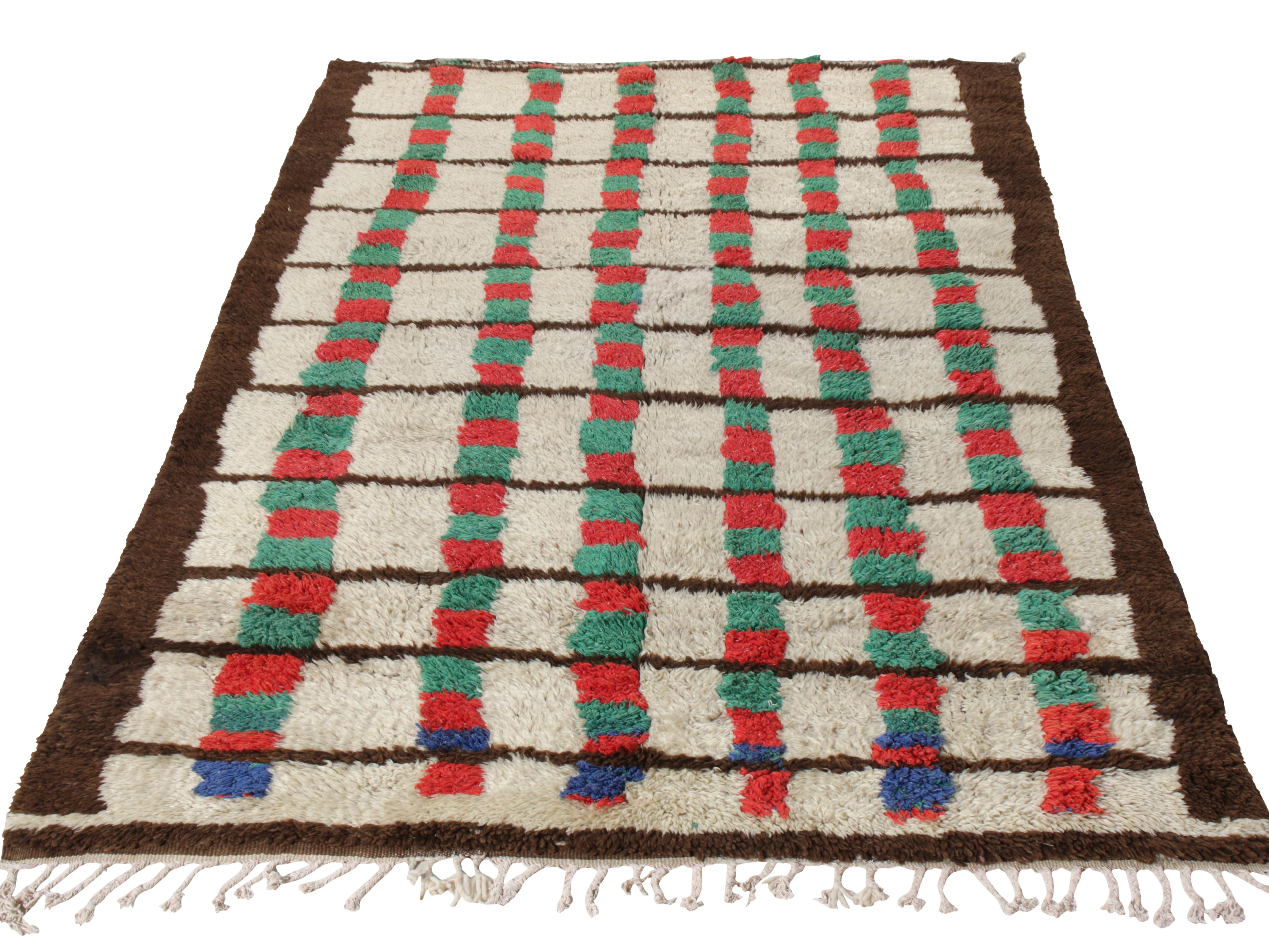 Hand knotted in wool with a high-low style from Morocco circa 1950-1960, this vintage 5x7 Moroccan rug is an exemplary piece in a multicoloured striped pattern. Playful hues of red and green sit comfortably on a beige-brown field, fabulously playing