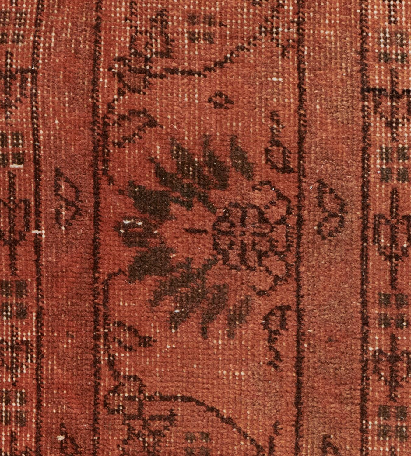 This vintage Turkish rug has a terracotta-red field with an overall design of faded chocolate-brown palmette and floral vine, in a terracotta-red border of meandering palmette and boteh vine, between narrow floral vine stripes.