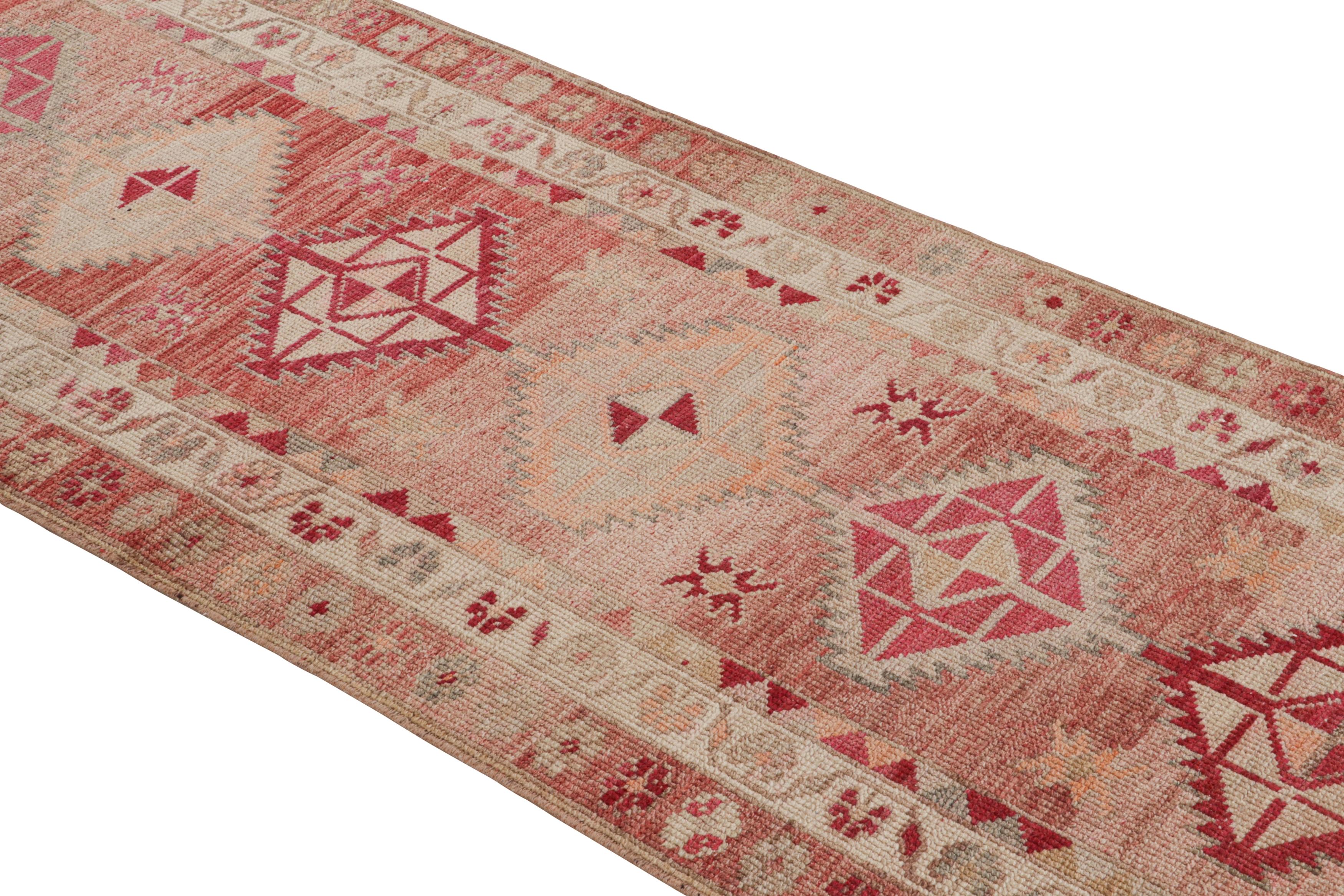 Hand knotted in wool originating from Turkey circa 1950-1960, this 3x12 vintage runner connotes a mid-century tribal rug design of intriguing colorway diversity, playing lively, unique accents against an abrashed striation of red and pink tones for