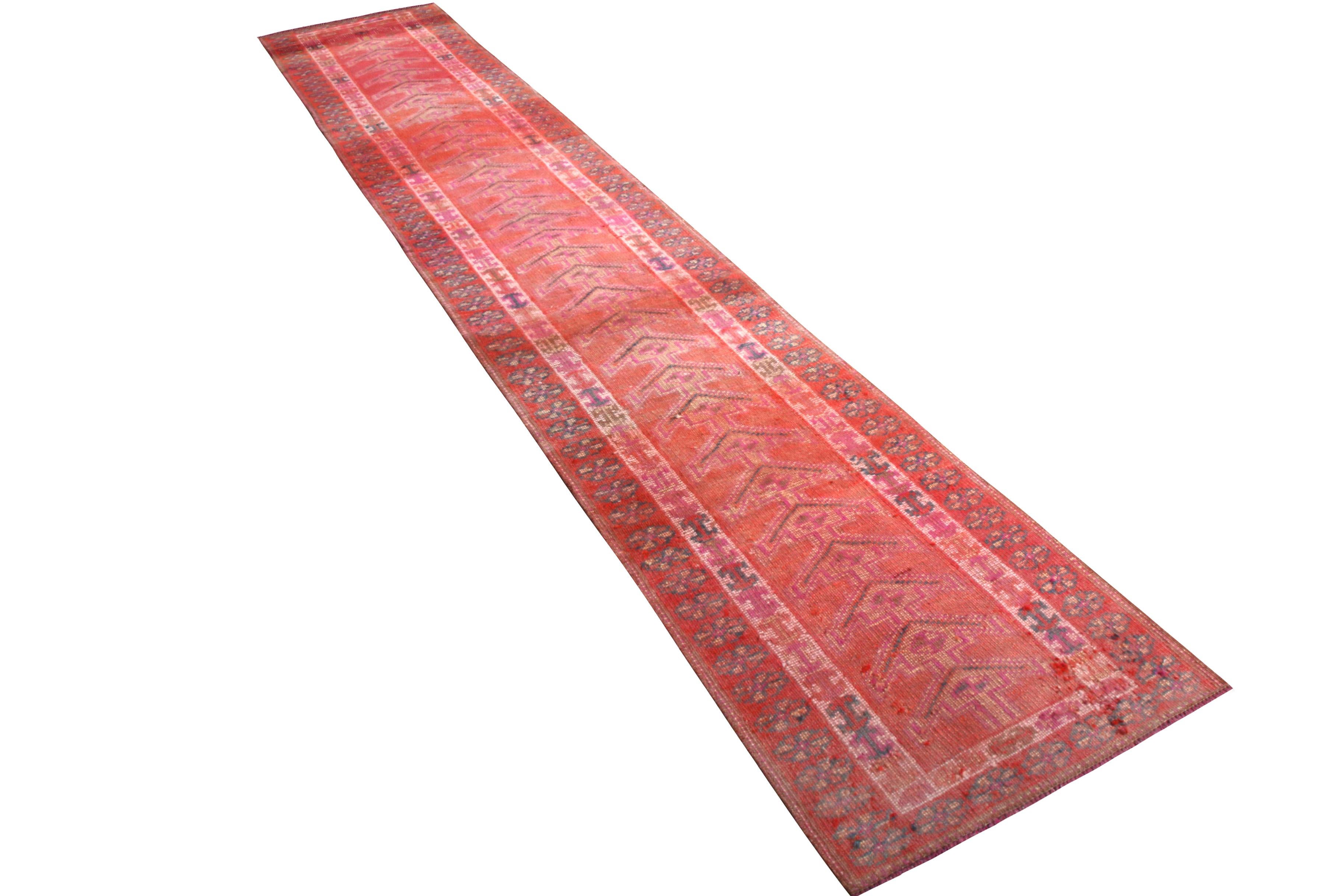 Hand knotted in wool originating from Turkey circa 1950-1960, this 2 x 14 vintage runner remarks a distressed mid-century tribal rug of rich red, incorporating prevalent pink among the lively accenting colorways bringing out the inviting repetition