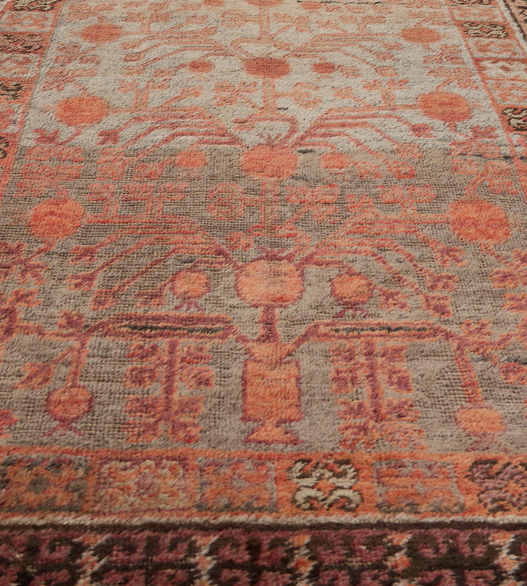 This antique Khotan runner has a shaded steel-blue field with an overall design of terracotta-red angular pomegranate vine, in a border of linked square panels each with a hooked floral motif, outer light purple linked hooked floral motif stripe.