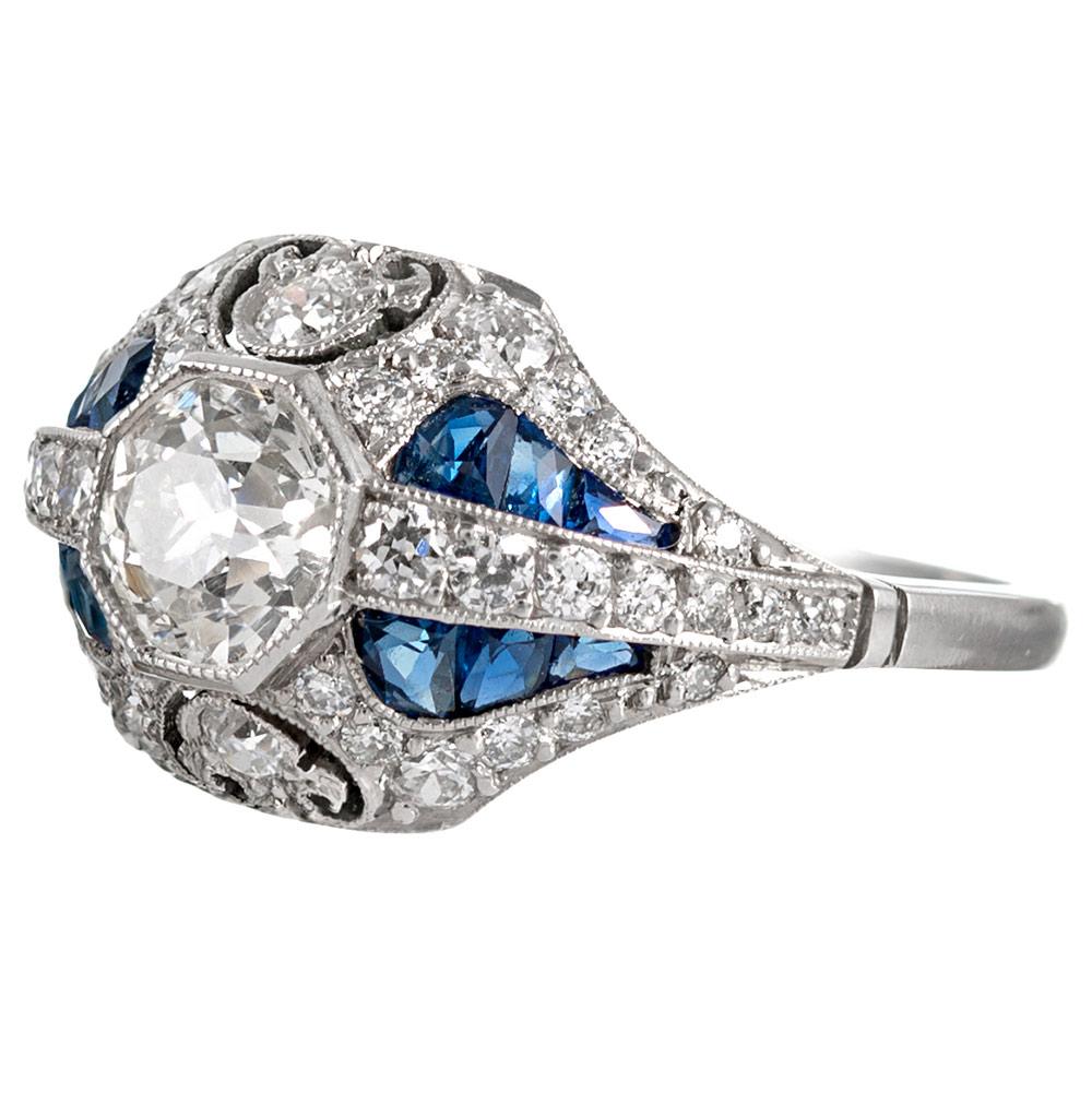 Detail abounds from every angle on this hand made platinum art deco inspired ring. With a .93 carat J/I1 diamond set in the center, the impact of the ring is augmented by an additional .50 carats of white diamonds and custom-cut sapphires. Note the