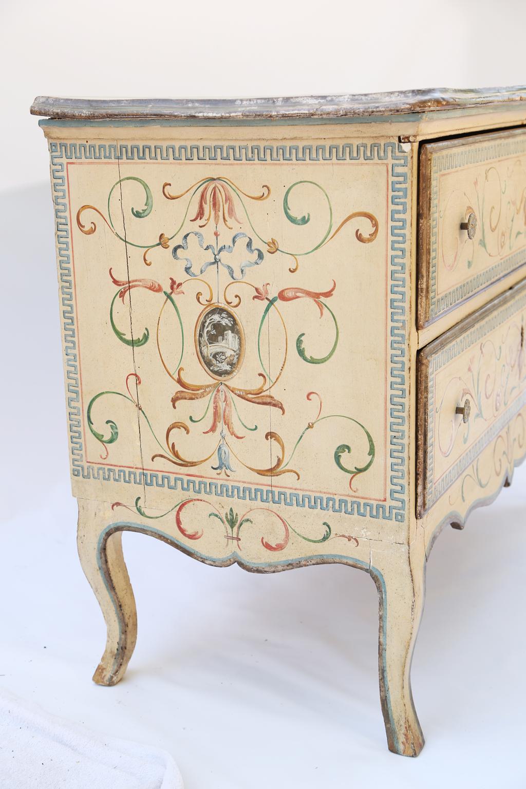Period commode, having a painted and parcel gilt finish, its rectangular molded top, with shaped front, over double stacked drawers, its serpentine stretcher raised on cabriole legs, the entire piece hand-painted with classical motifs of scrollwork