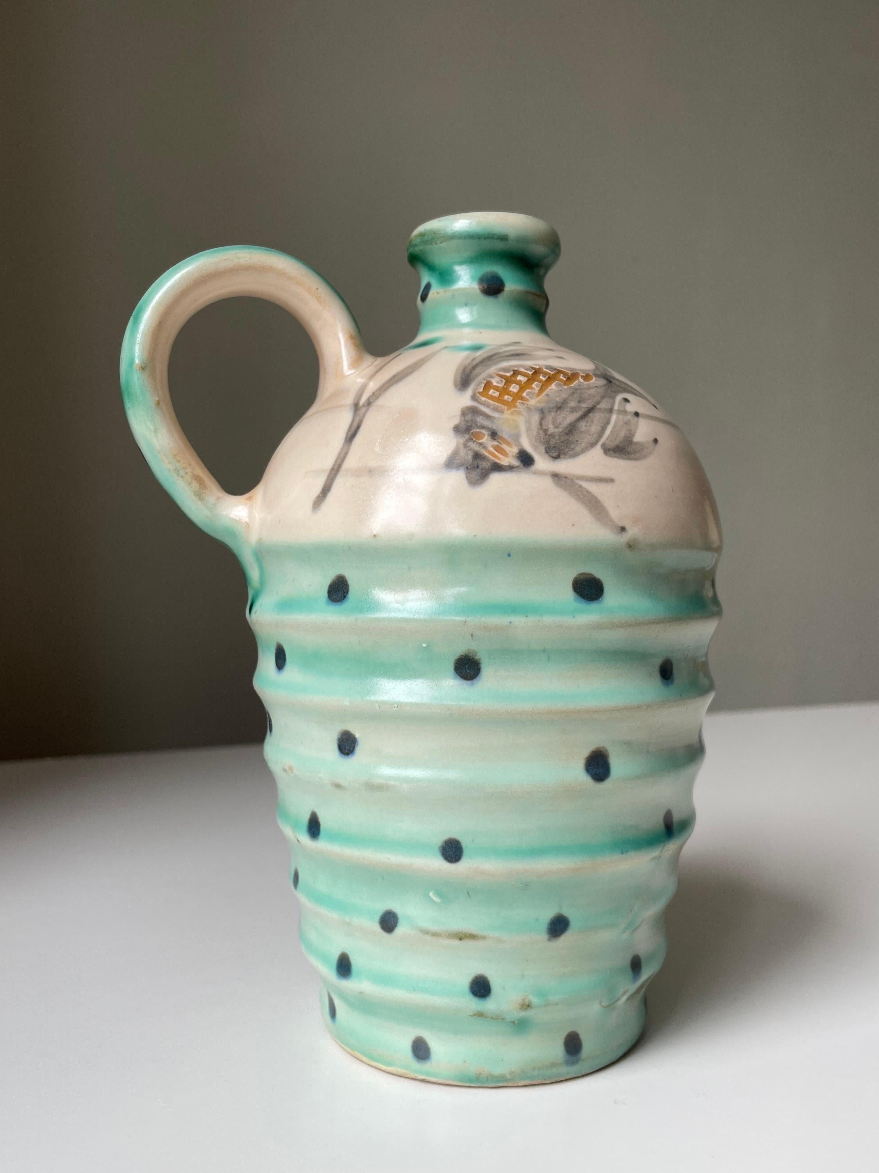 Hand-painted Danish organic modern ceramic pitcher bottle vase with large handle on one side. Rippled body with slender neck and bright sea green glaze with large anthracite dots. Large light gray and brown relief striped fish with lined sea grass