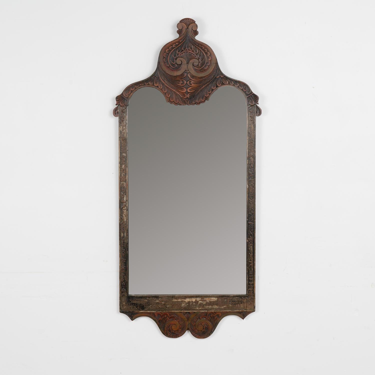 The attractive carving found in the frame of this mirror includes dramatic flourishes on top, balanced at the base while narrow sides contain figures, birds and more. 
Notice the original brown/black painted finish shows residual touches of red and