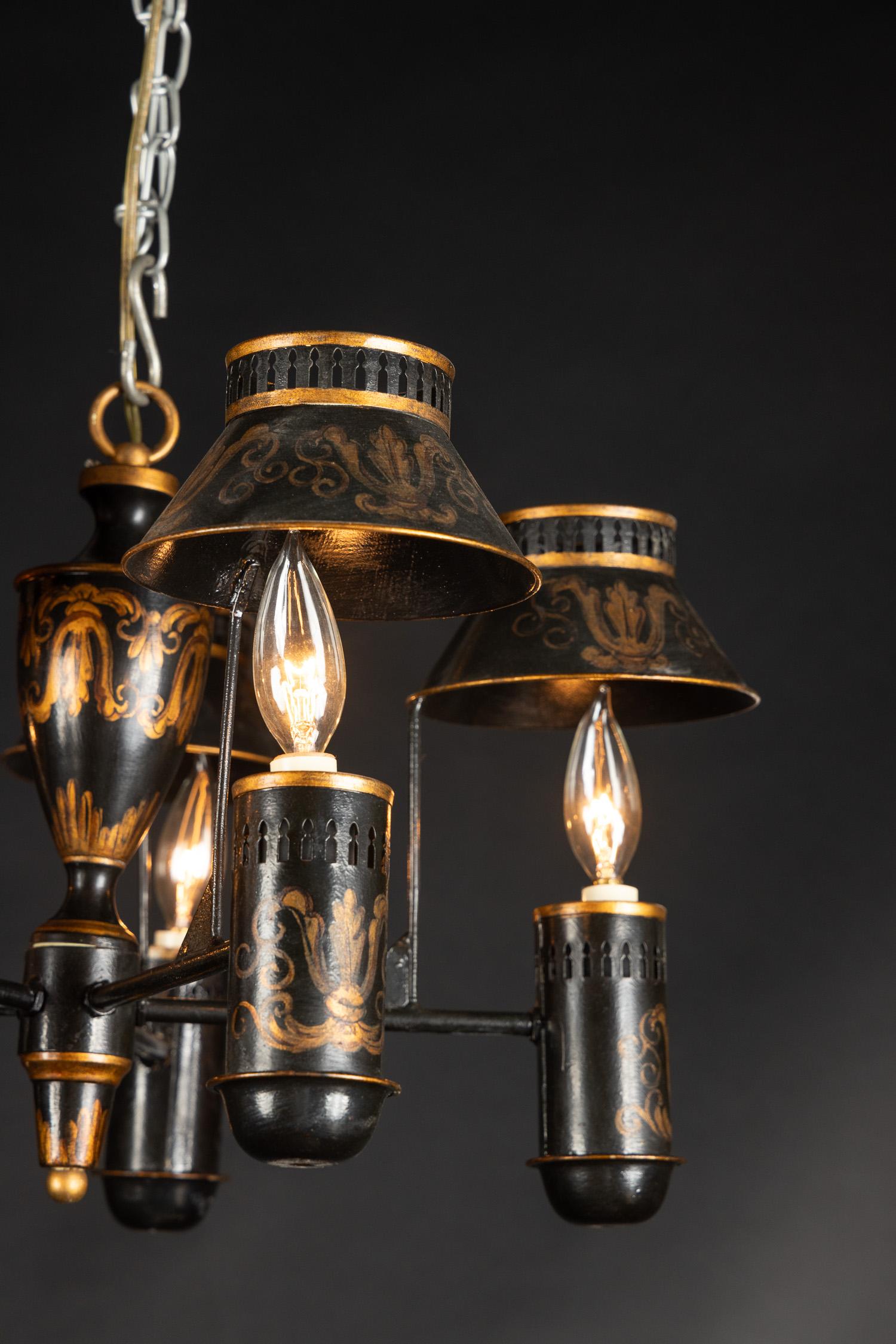 Ce magnifique lustre français à six lumières est fait de tole (étain) et date du milieu du 20e siècle. Le luminaire est peint à la main avec des volutes délicates et comporte des abat-jour au-dessus de chaque lampe. Les abat-jour sont percés en