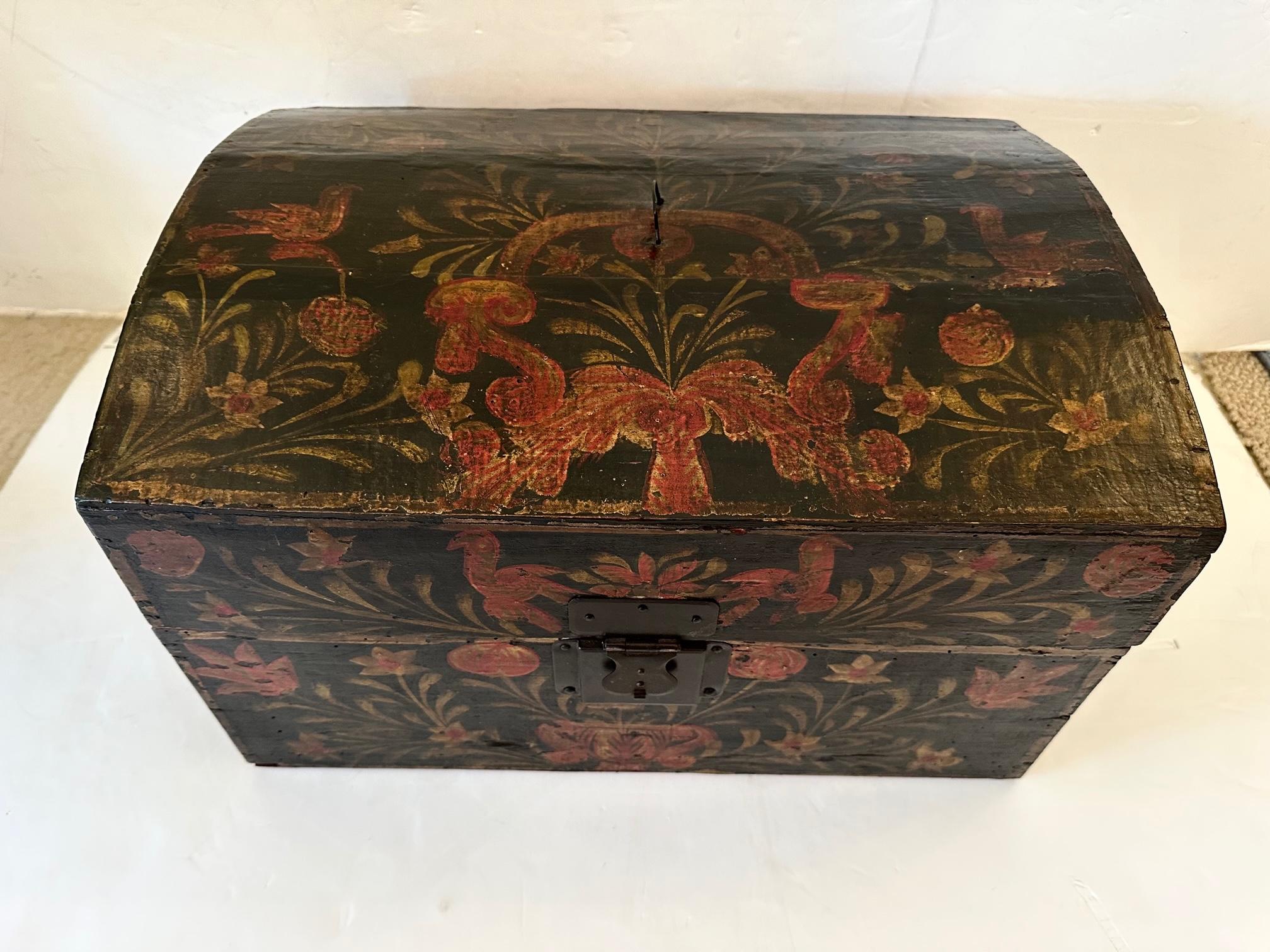 Gorgeous antique hand painted folk art treasure box having black background with red and green rustic decoration, original lock with key, and red interior.