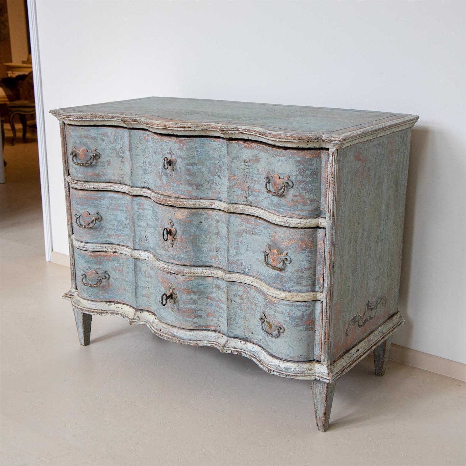 Baroque chest of drawers on square legs with a serpentine front and three drawers. The setting in light blue is new and decoratively rubbed through, the trusses are set off in white-beige.
   