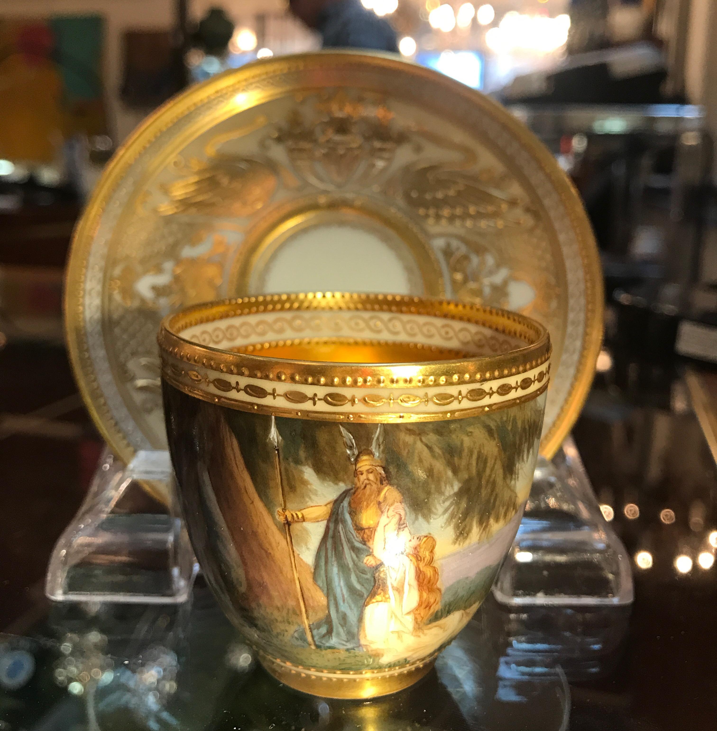 A fully hand painted and hand gilt demitasse cup and saucer. This is highly detailed for its small size and skillfully decorated all around with lavish gilt interior and raised gilt saucer original to the cup. The panoramic view represents Wotan &