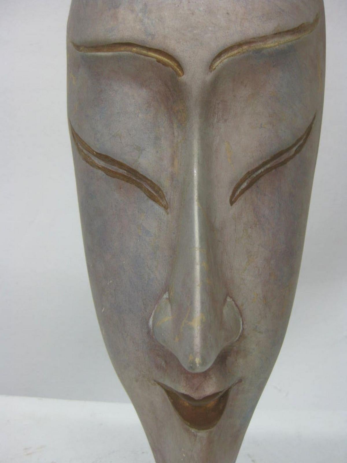 This hand-painted mask features a female long face. Gold accents that highlight lips and eyes suggest Japanese culture.
It is resting on a clear Lucite-mounted base.