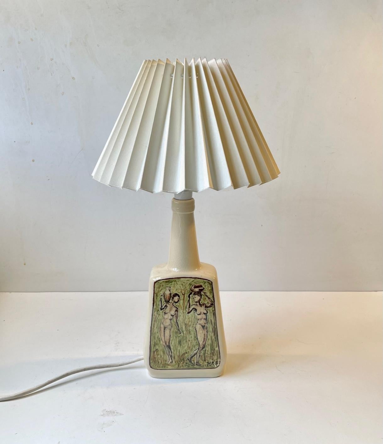 Skillfully hand-painted ceramic table light with a creamy pastel main-glaze. The front motif signed H.R.S (unknown artist - German or Danish) depicts two water jug carrying woman in a green field. With bulb the light measures 35 cm in height. The