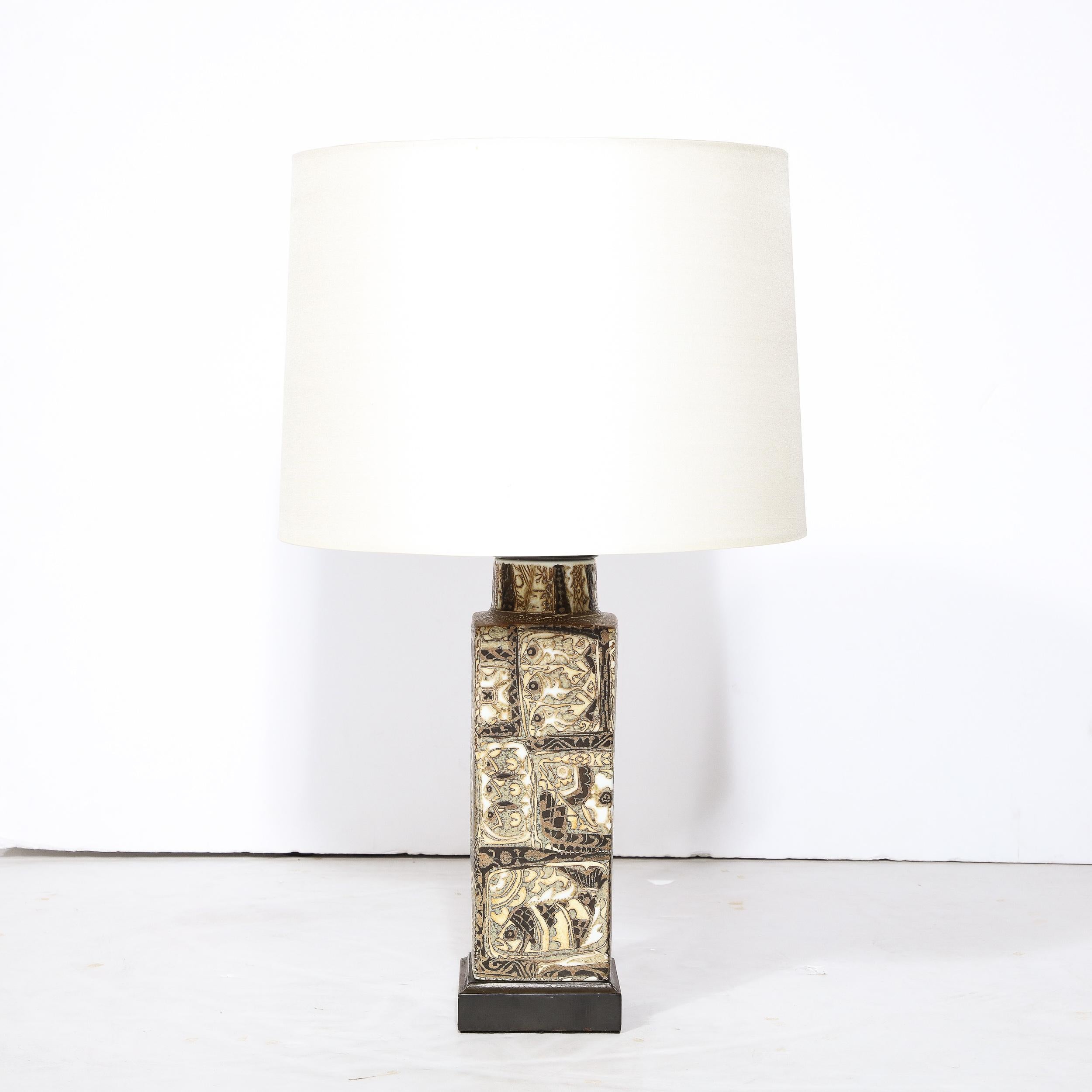 This refined Mid-Century Modern ceramic table lamp was realized by the illustrious studio of Royal Copenhagen in Denmark circa 1950. It features a square black enamel base that ascends into a rectilinear volumetric body and tapered neck. From a