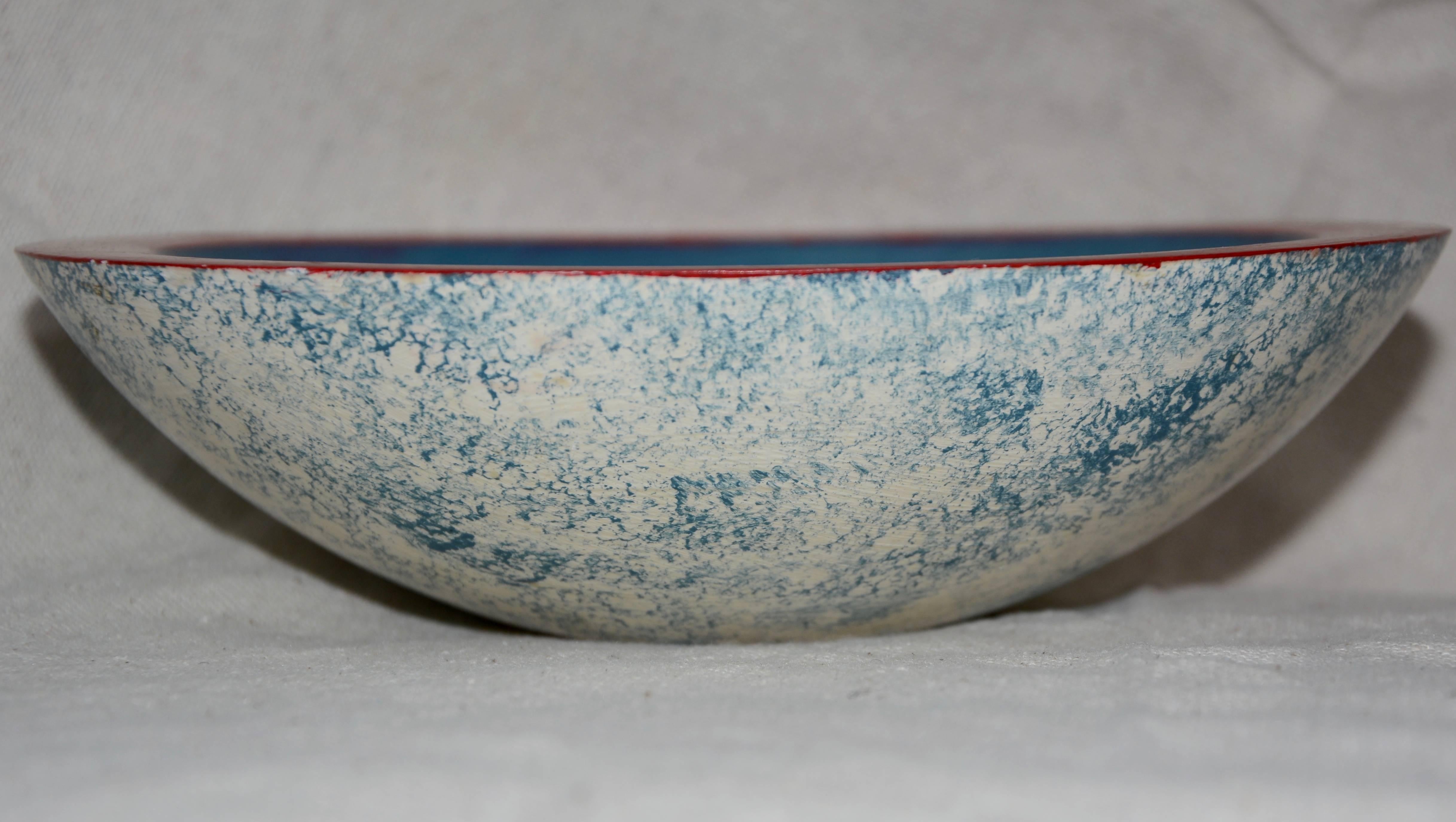 This is a unique wooden hand painted bowl. This hand painted wooden bowl features a red rim with a white chicken on a blue background. The exterior of the bowl has a blue and white sponged finish. The bowl is marked to the underside with Christ