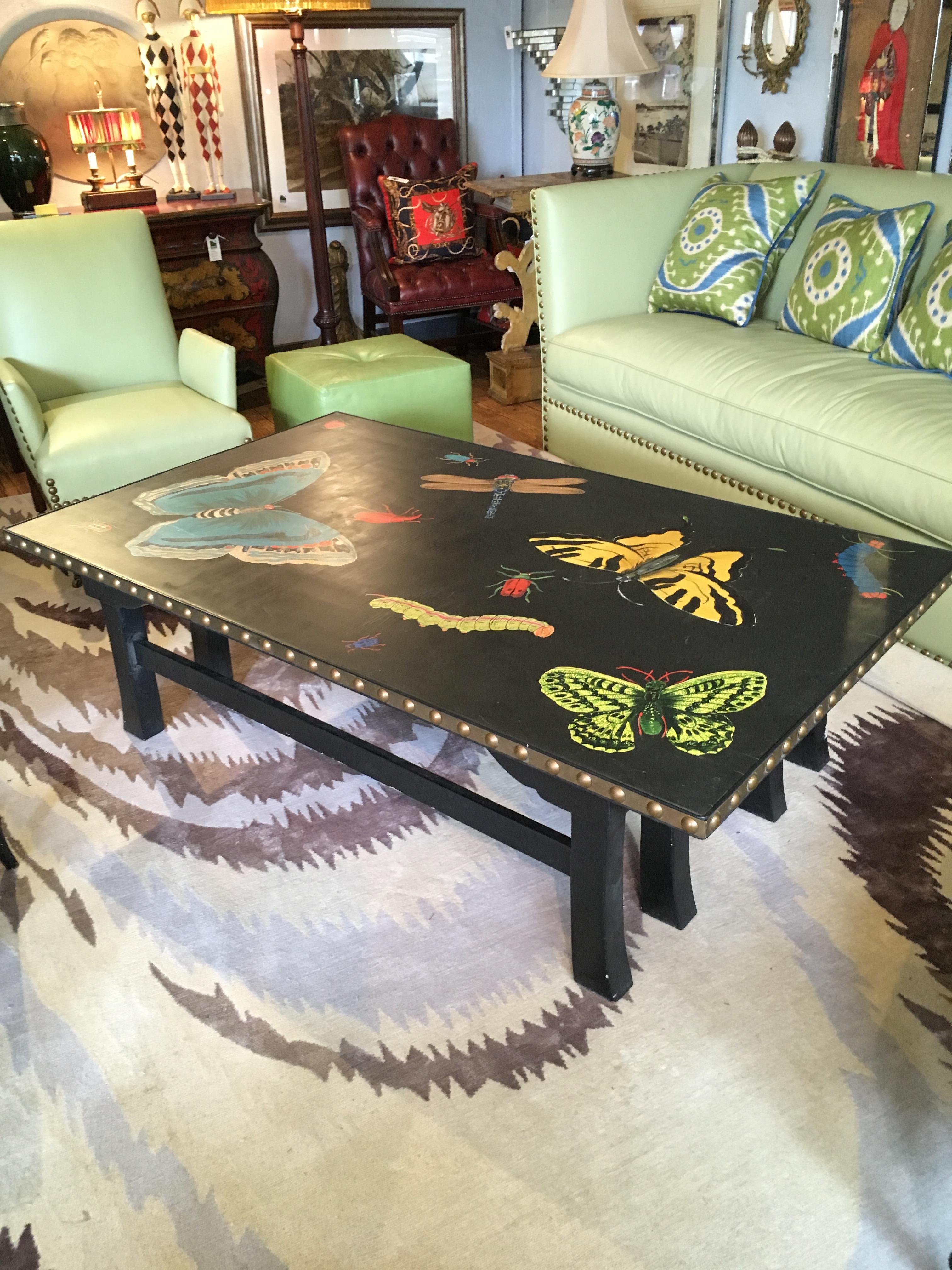 A sensational hand painted rectangular coffee table having boldly rendered bright butterflies, dragonflies and lady bugs against a black background and finished with big brass nailheads.