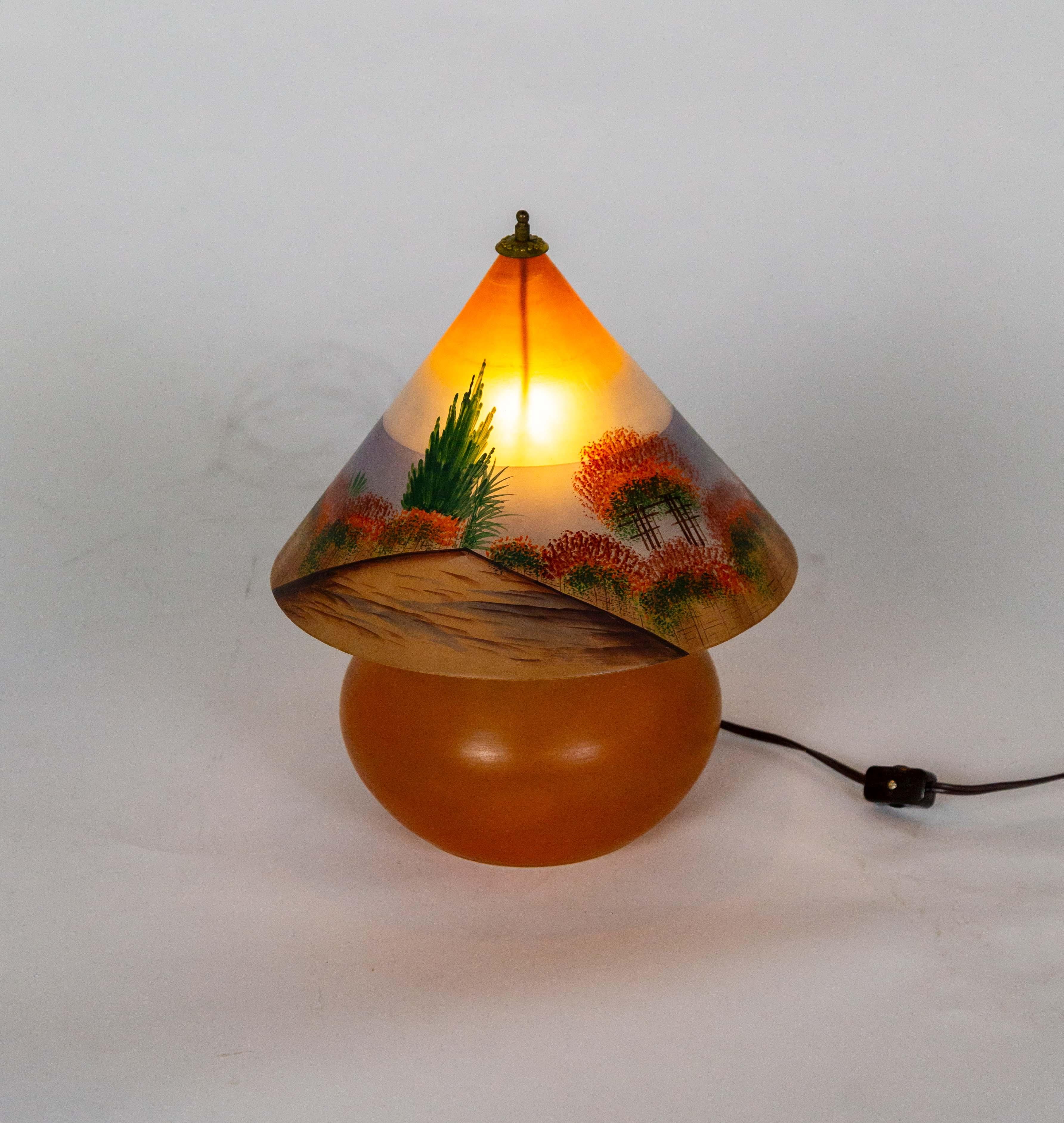 Eine handgefertigte tschechoslowakische Glastischlampe mit kugelförmigem Fuß und kegelförmigem Schirm.  Der Schirm hat eine handgemalte Landschaft in Orange und Blau mit rotem und grünem Laub und sieht bei Beleuchtung wie ein Sonnenaufgang aus. Der