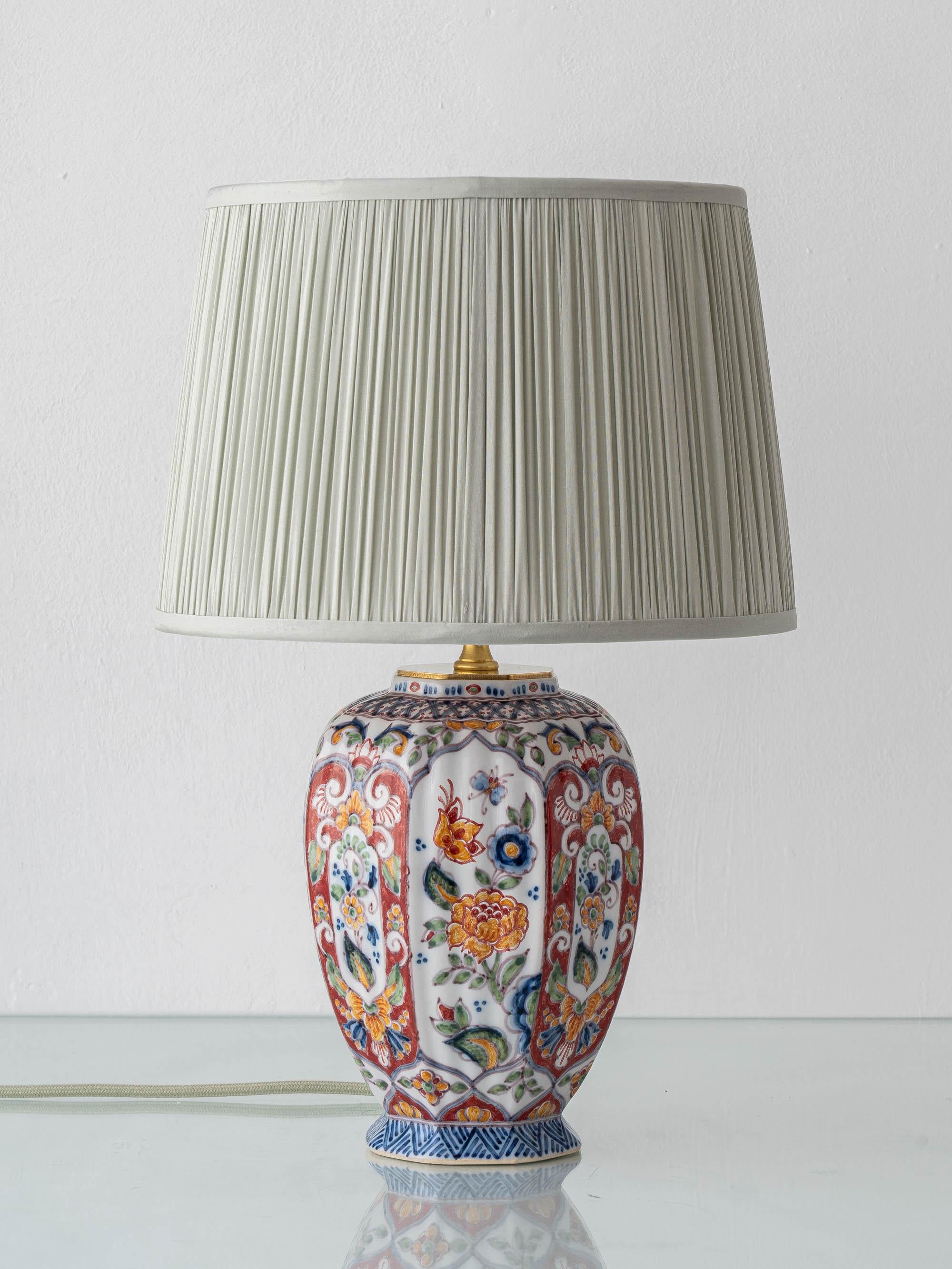 Meticulously handcrafted by Amitābha Studio from an antique Altena & Krooyenga Makkum (Netherlands, mid-20th century) earthenware vase— hand-painted in polychrome Delftware style—paired with a pleated silk lampshade in light sage green.

This