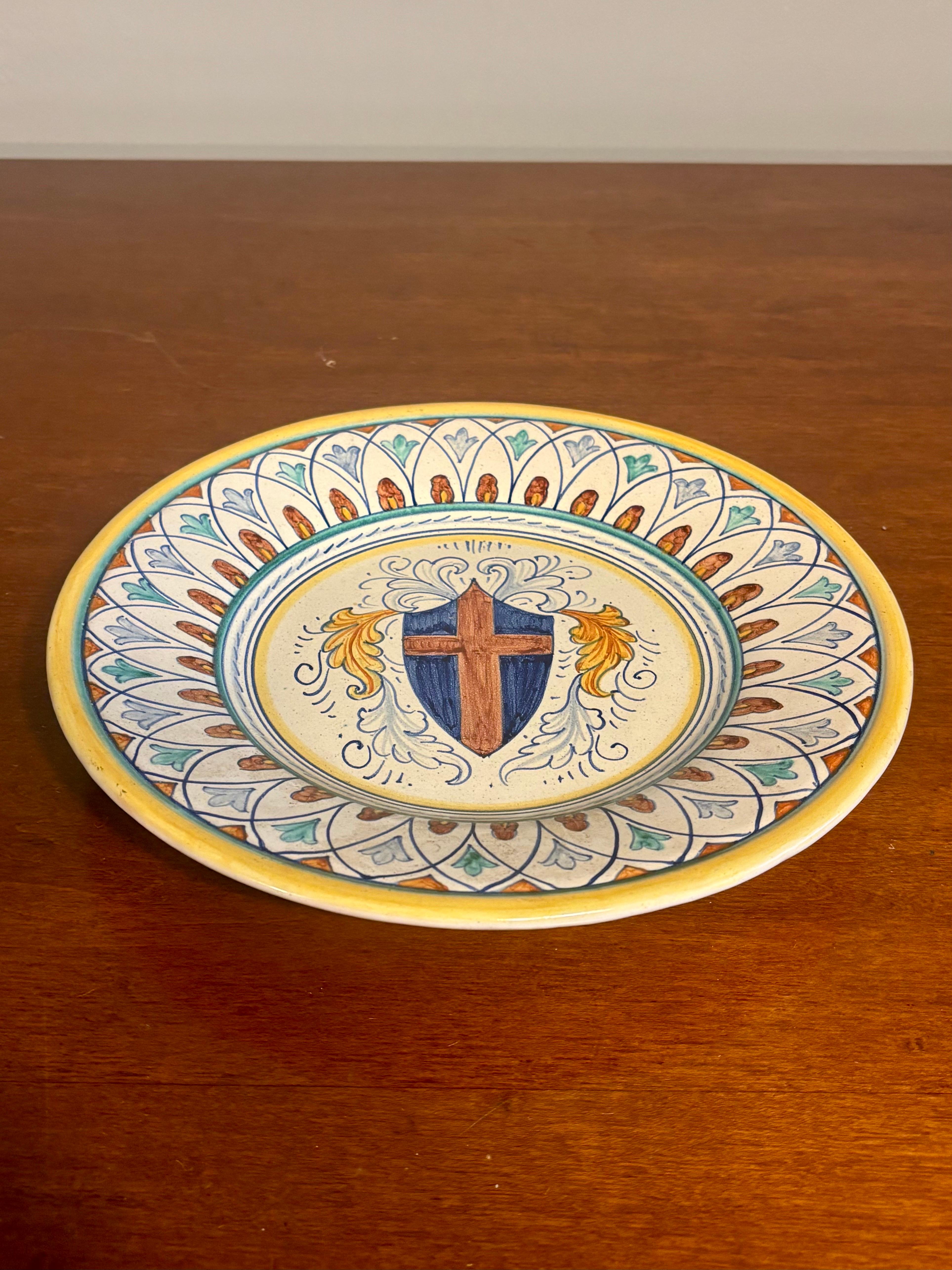 Cette élégante assiette murale de Deruta présente un blason héraldique finement rendu, exécuté dans une magnifique palette de bleu, d'ocre, de jaune, de sarcelle et de tons bruns-orangés doux. Le design reflète l'élégance durable de la majolique de